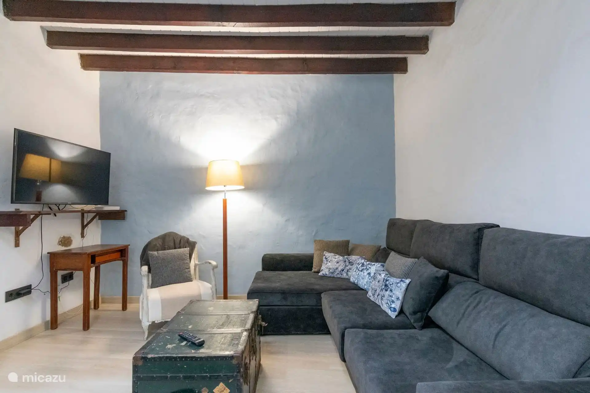 Salón con sofá rinconero, televisión y baúl antiguo.