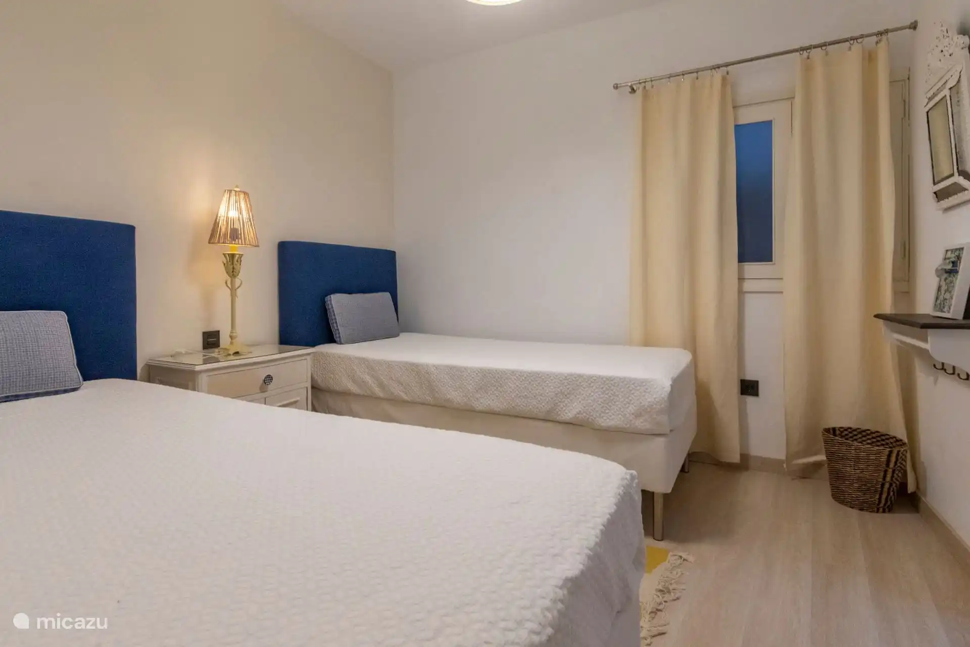 Vista del dormitorio de dos camas con lámpara y cortinas.