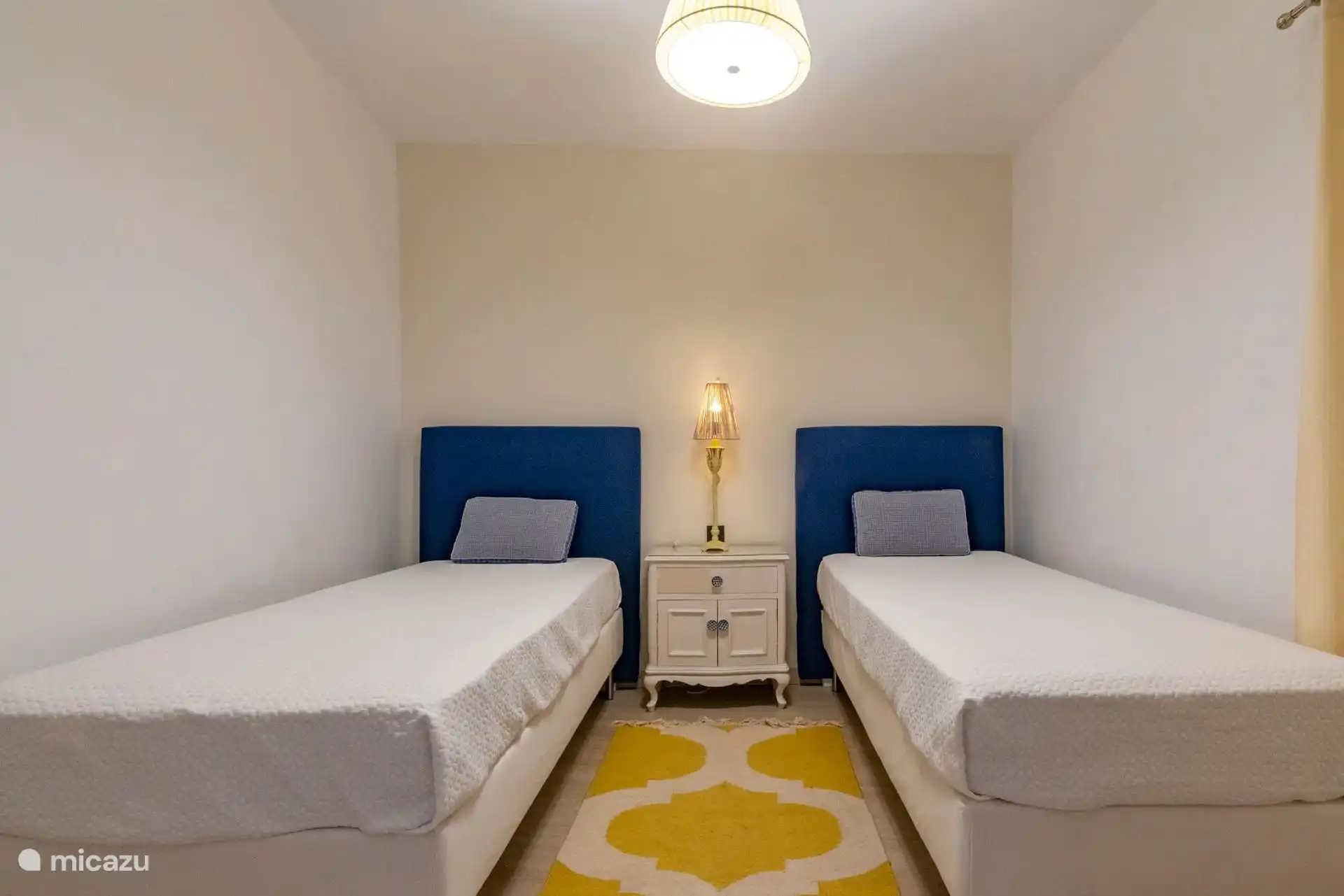 Dormitorio con dos camas individuales de cabecero azul y alfombra amarilla.