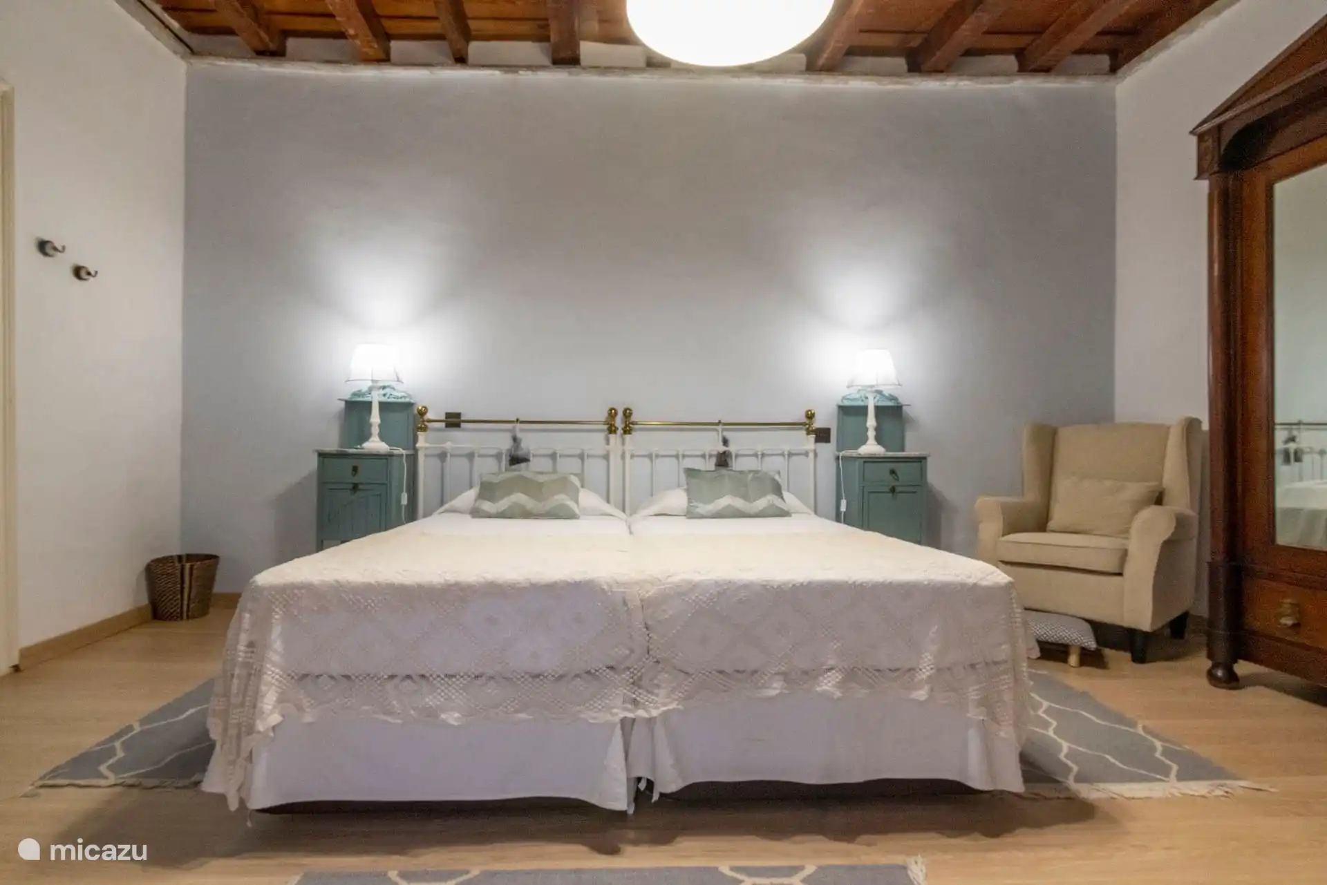 Dormitorio con cama de matrimonio, sillón y lámparas de pared.