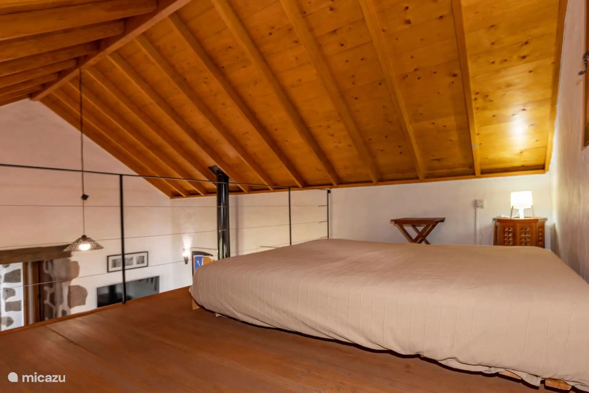 Altillo con cama doble bajo el techo de madera a dos aguas.