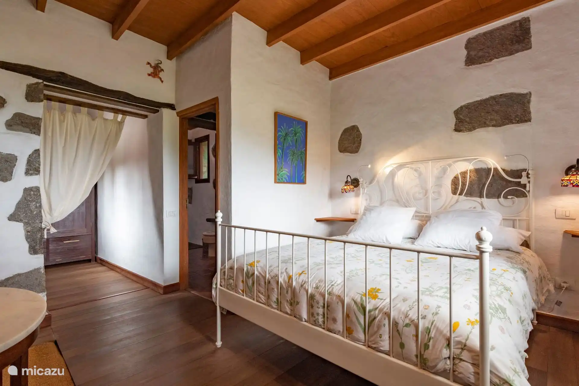 Dormitorio con cama doble de forja blanca y paredes de piedra.