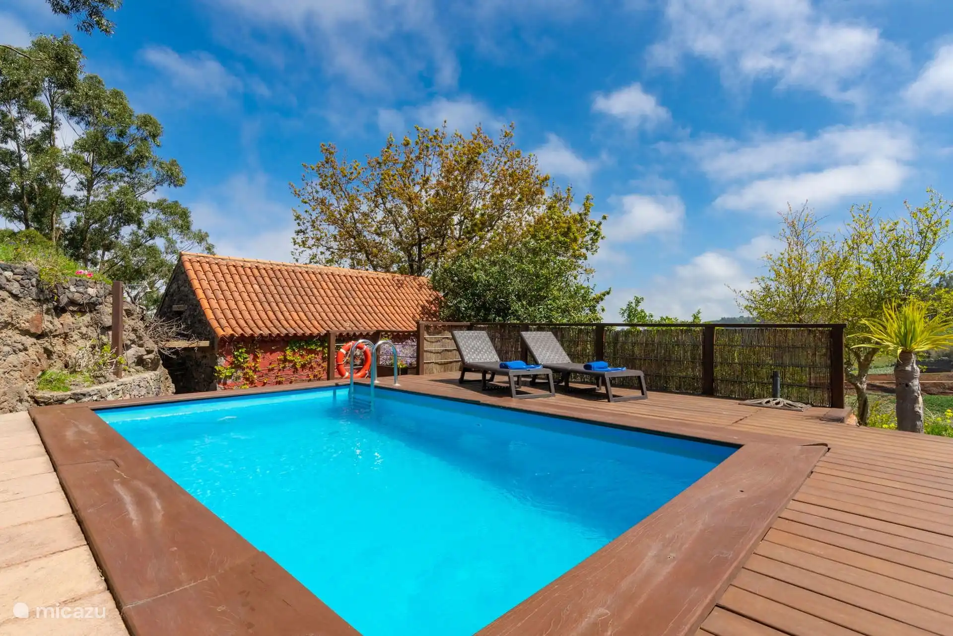 Piscina sobre tarima con tumbonas y valla de madera.