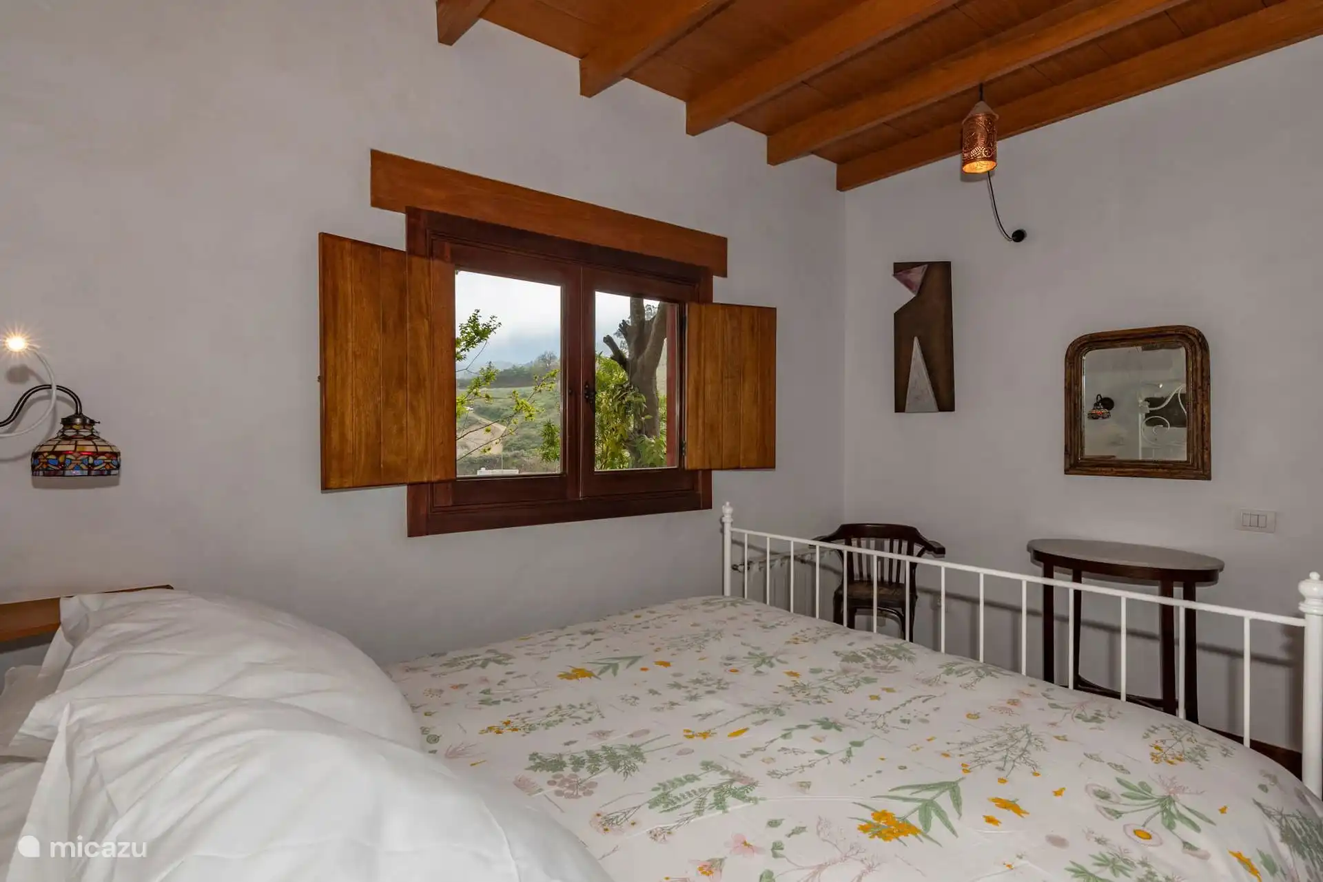 Dormitorio con la cama de forja junto a la ventana.