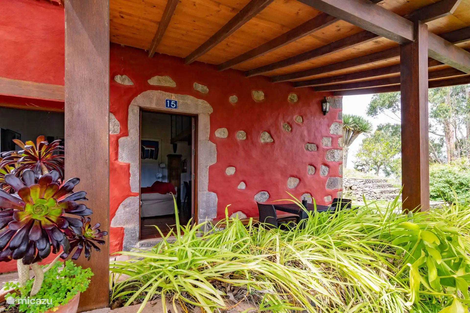 Entrada de la casa, con la pared roja y las piedras vistas.