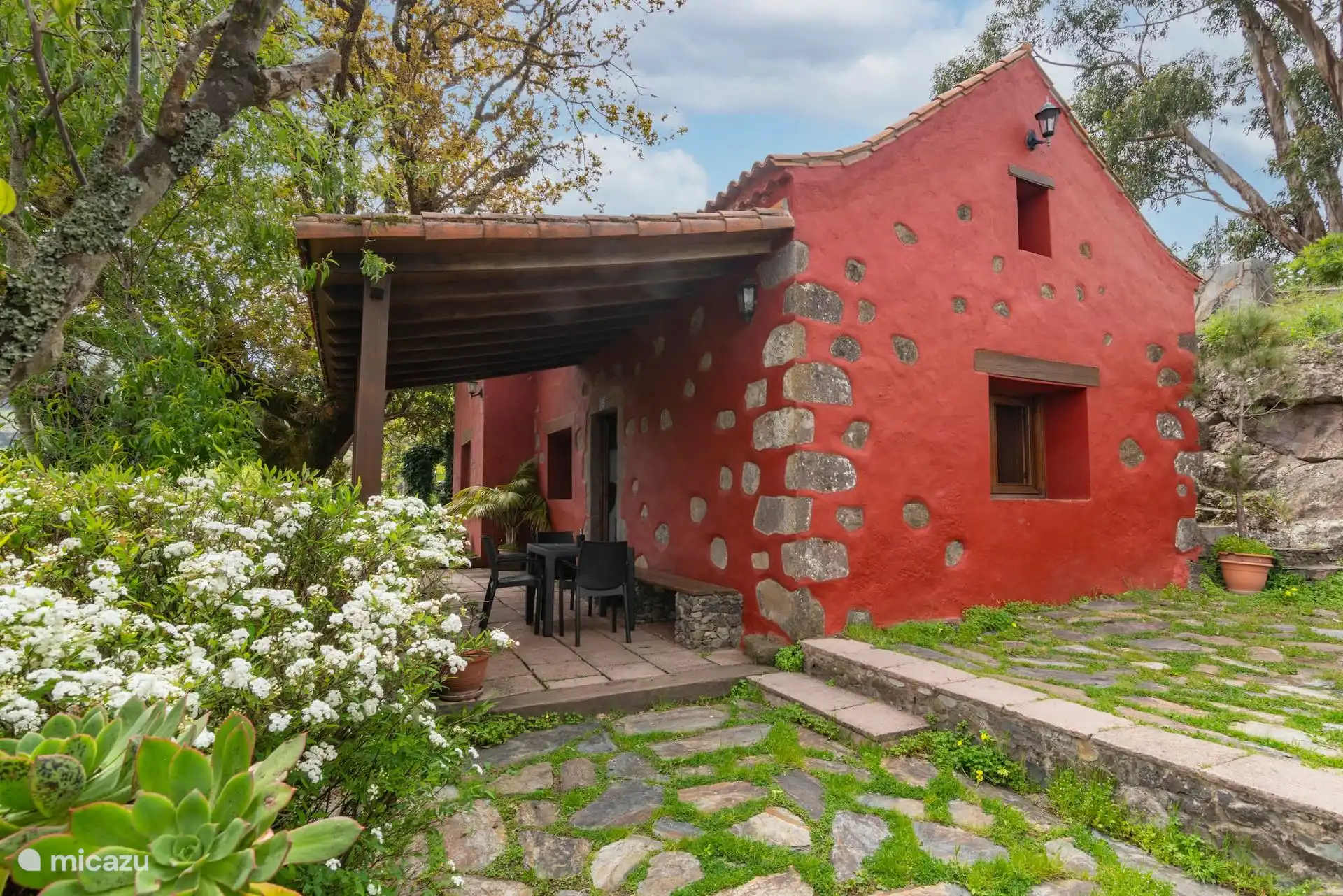 Fachada trasera con el porche y el jardín de flores.