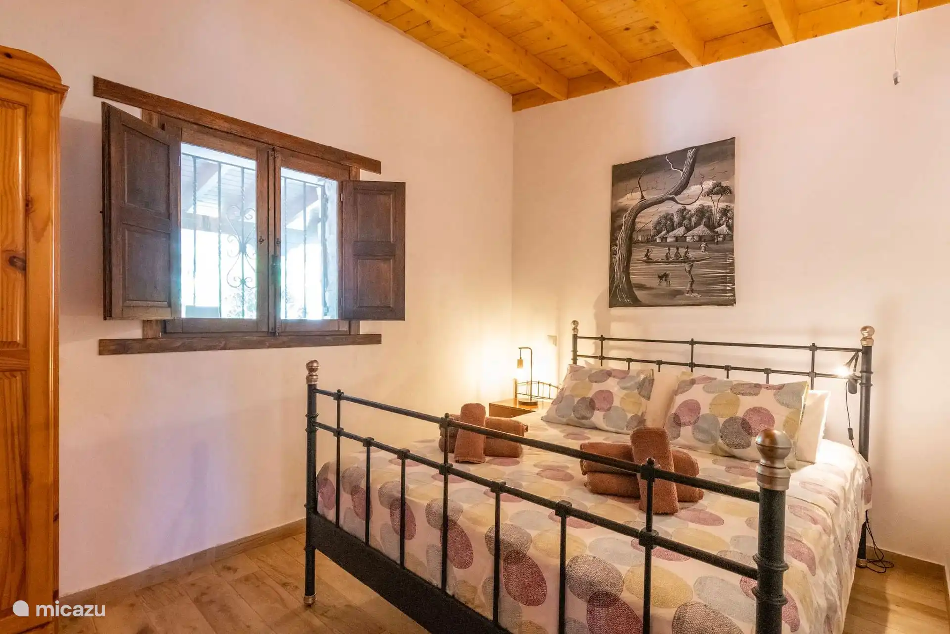 Schlafzimmer mit schmiedeeisernem Doppelbett und Holzdecke.