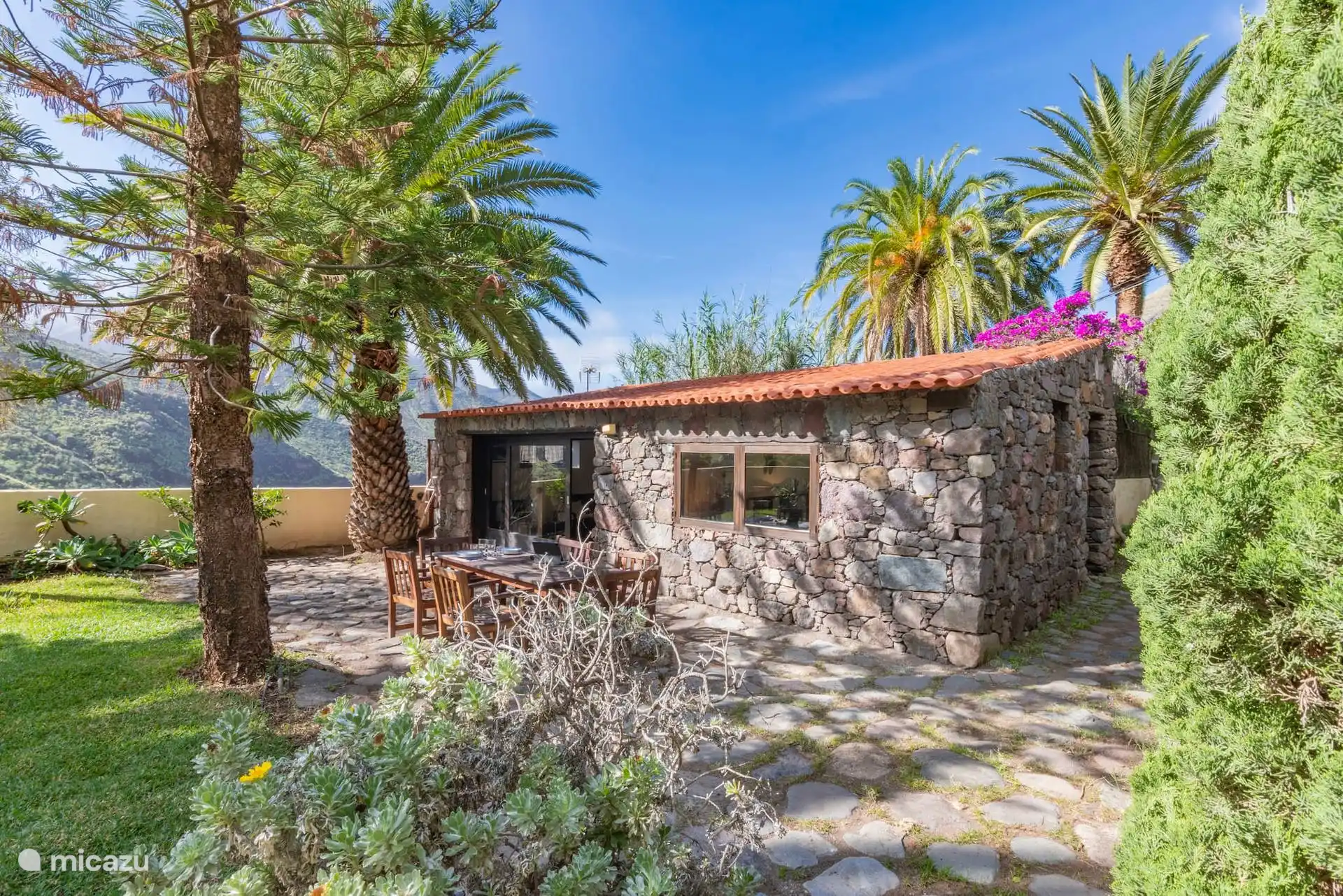 La casa de piedra entre palmeras y buganvillas.