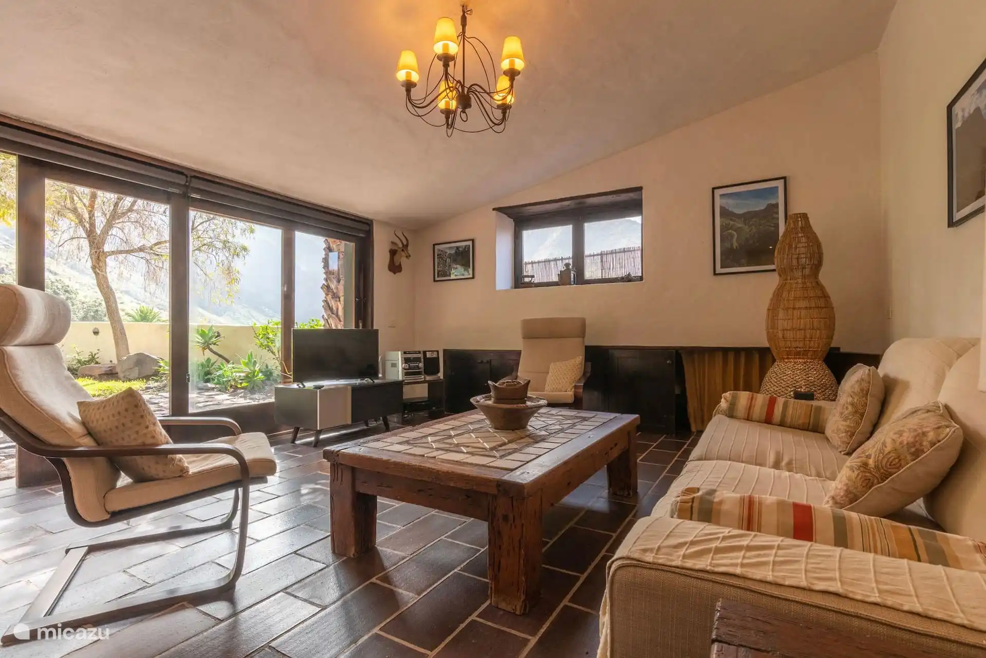 Salón con butacas, televisión y grandes ventanales al jardín.