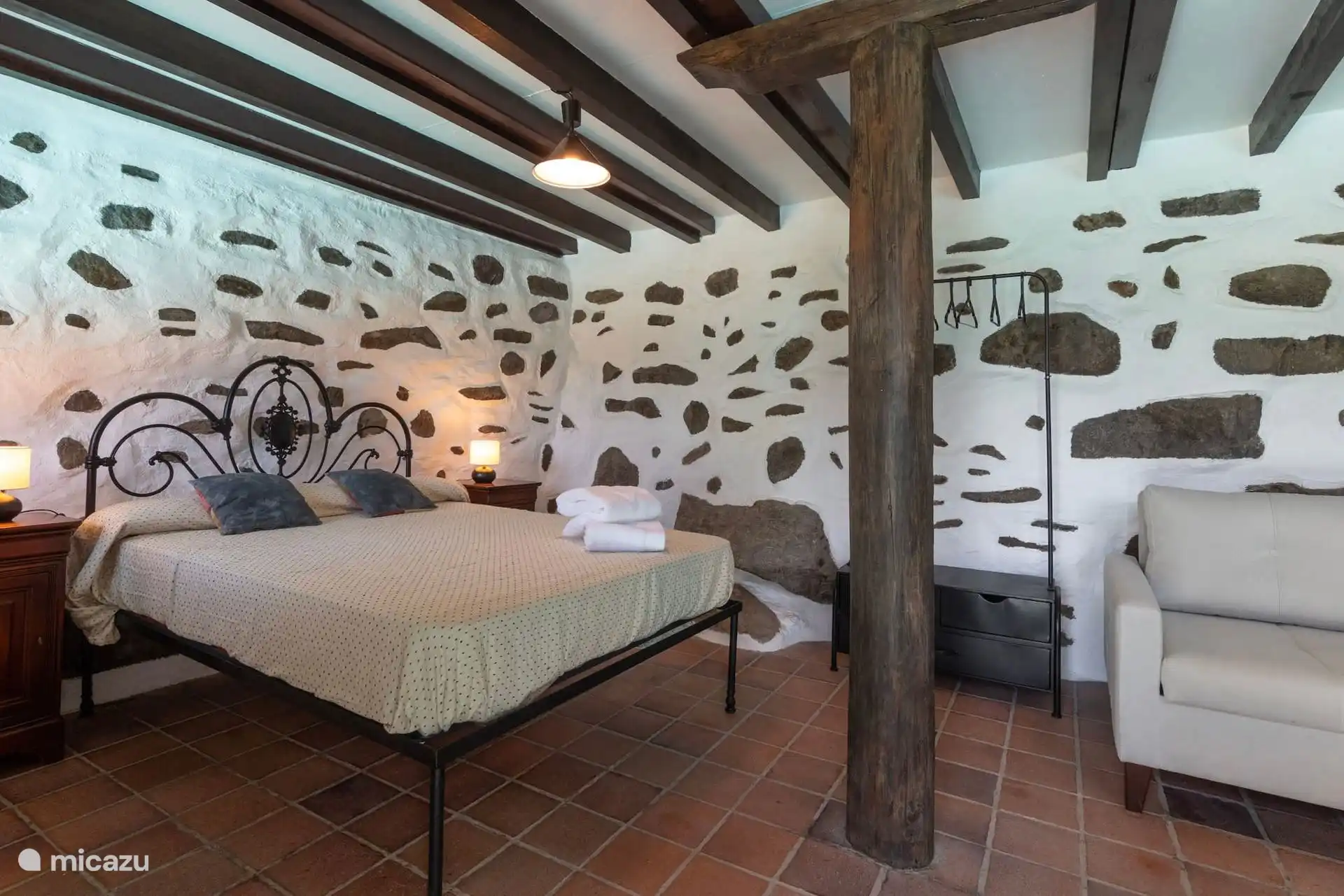 Dormitorio con muro de piedra y sillón de lectura.