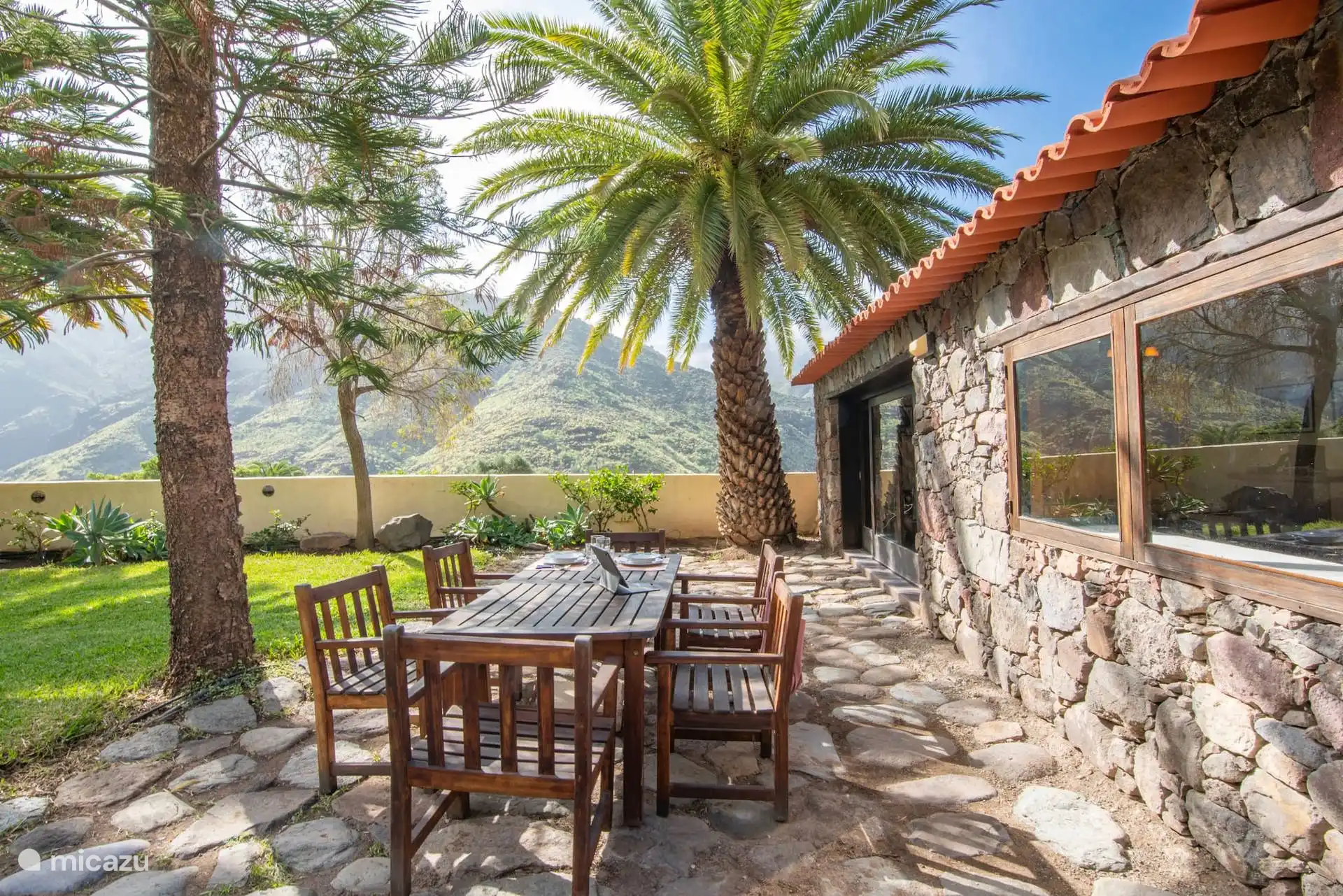 Terraza de piedra con mesa y sillas, entre palmeras.