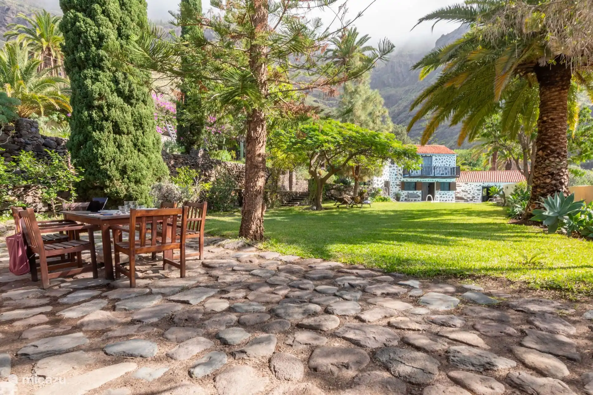 Jardín de césped con mesa de comedor exterior bajo los árboles.