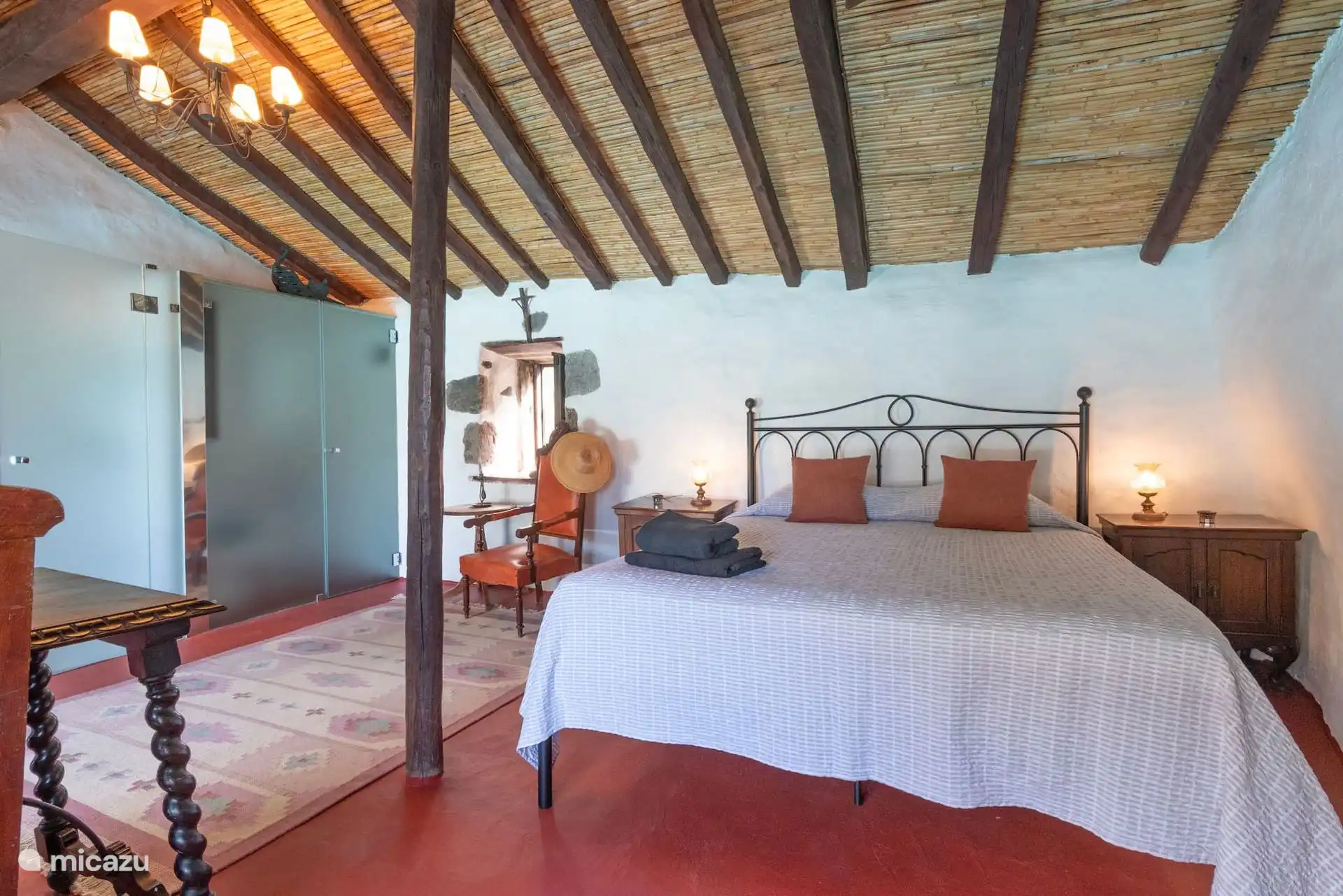 Dormitorio con cama de matrimonio de forja y techo de vigas.