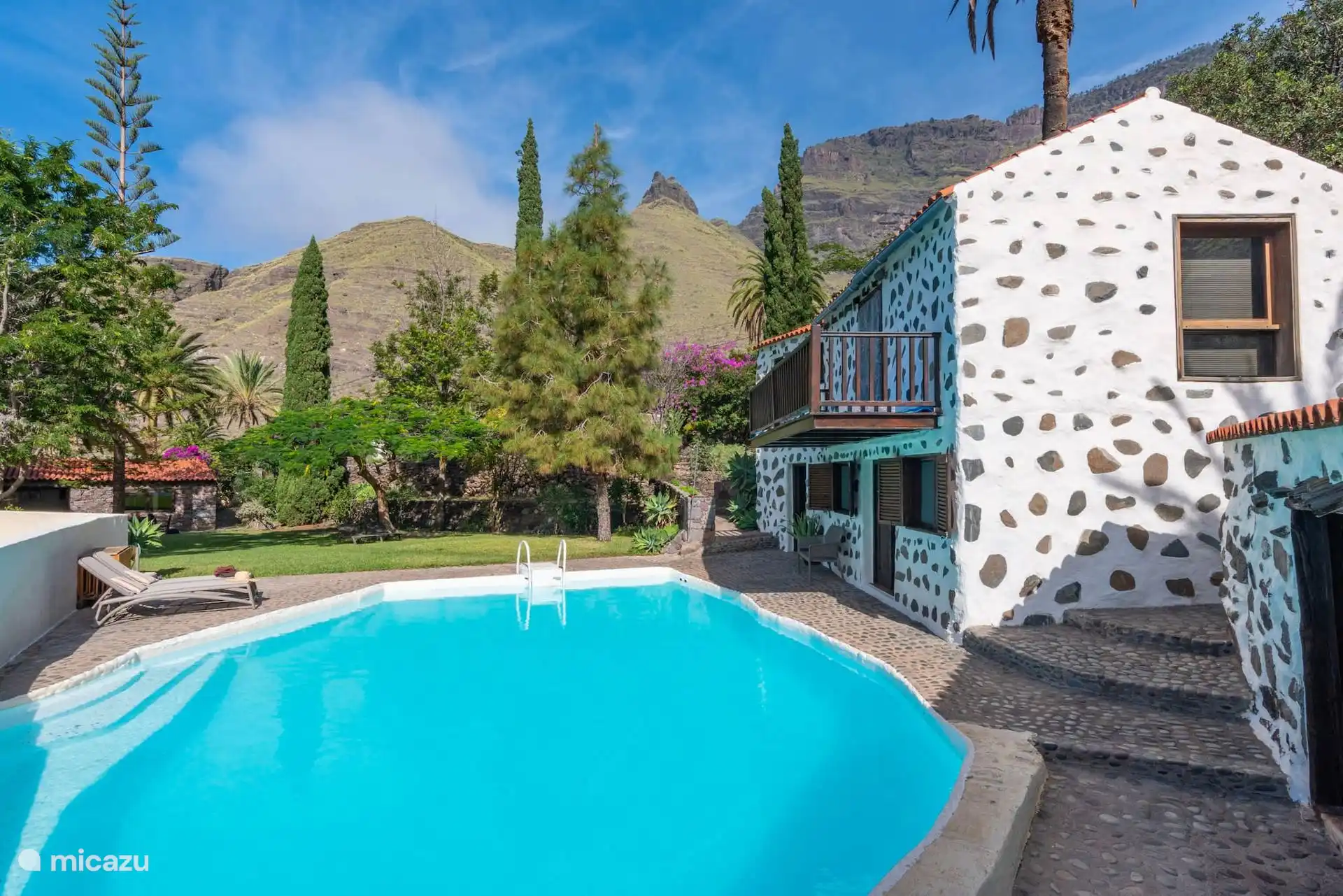 Piscina privada junto a la casa de piedra, con el risco al fondo.