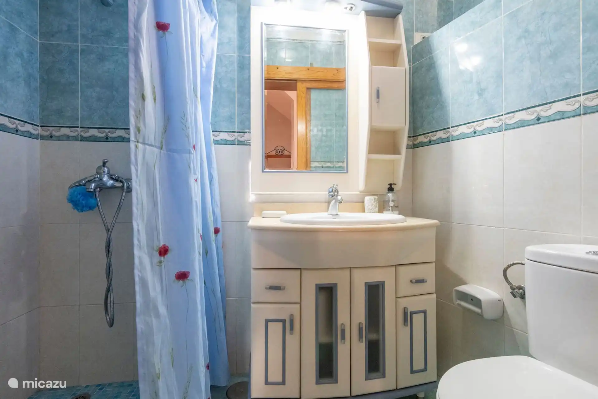 Badkamer met gordijn, douche, wastafel en blauwe tegels.
