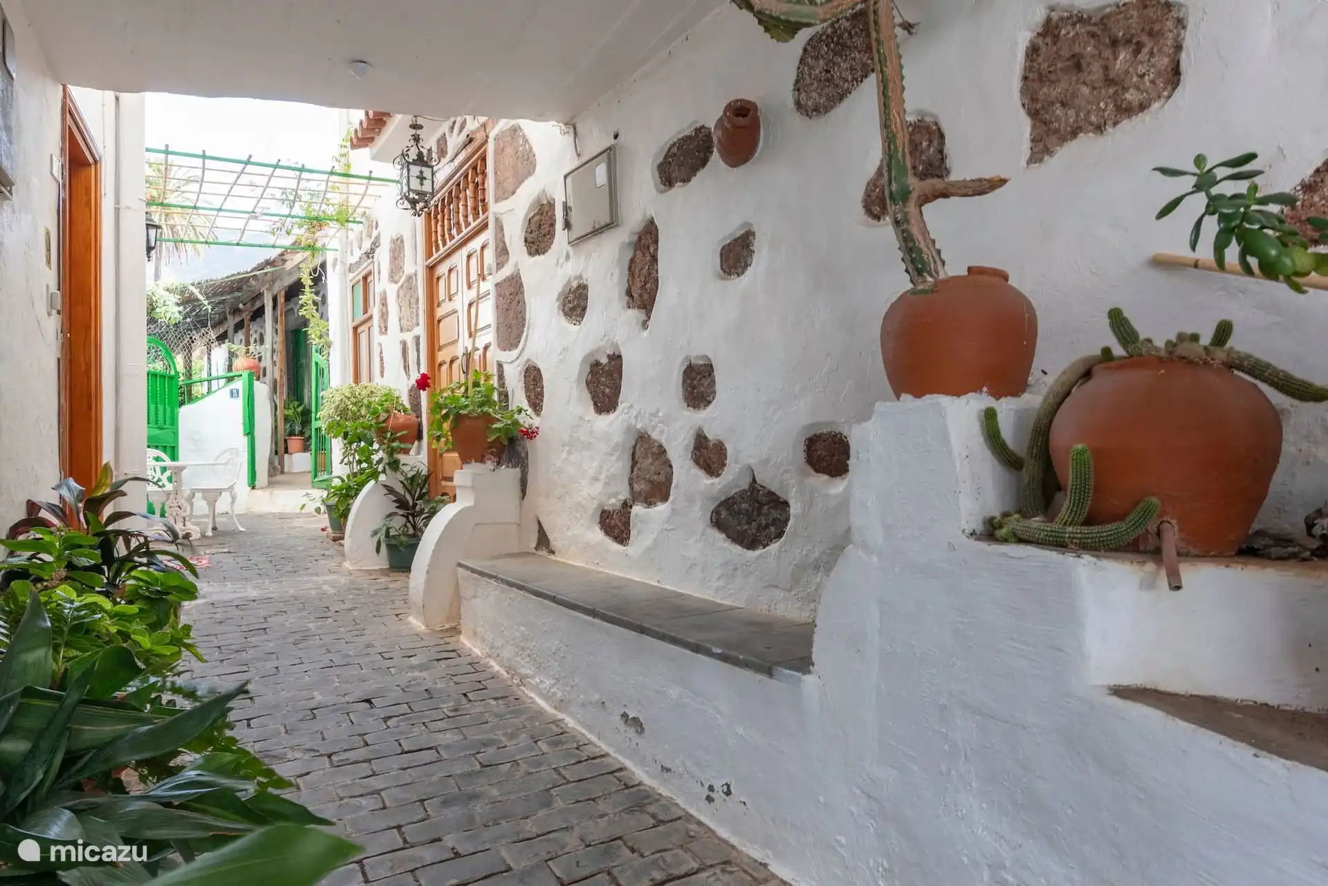 Witgekalkte steeg met bloempotten, bij de ingang van het huis.
