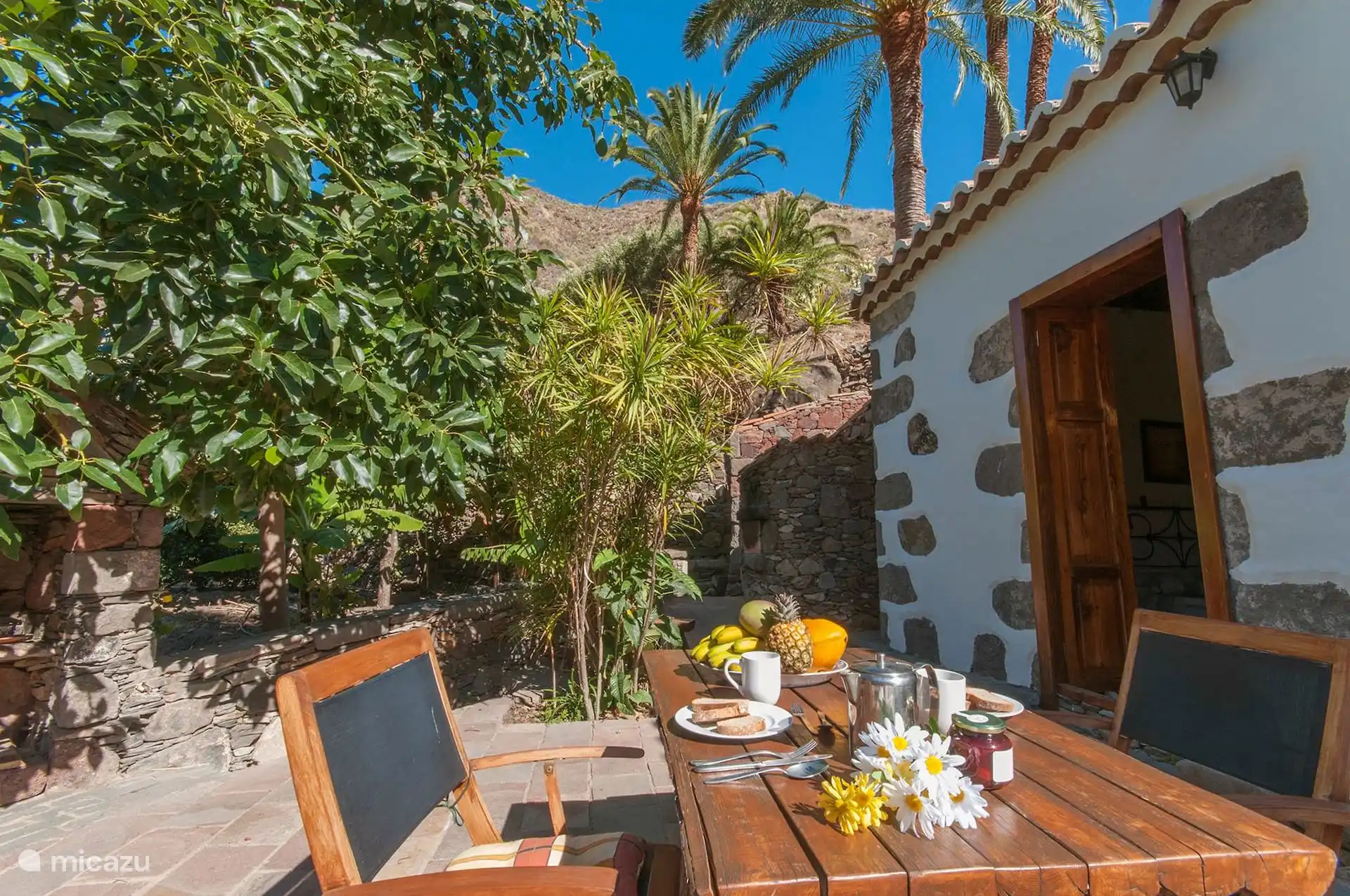 Terrasse mit Außen-Esstisch, neben dem Steinhaus.