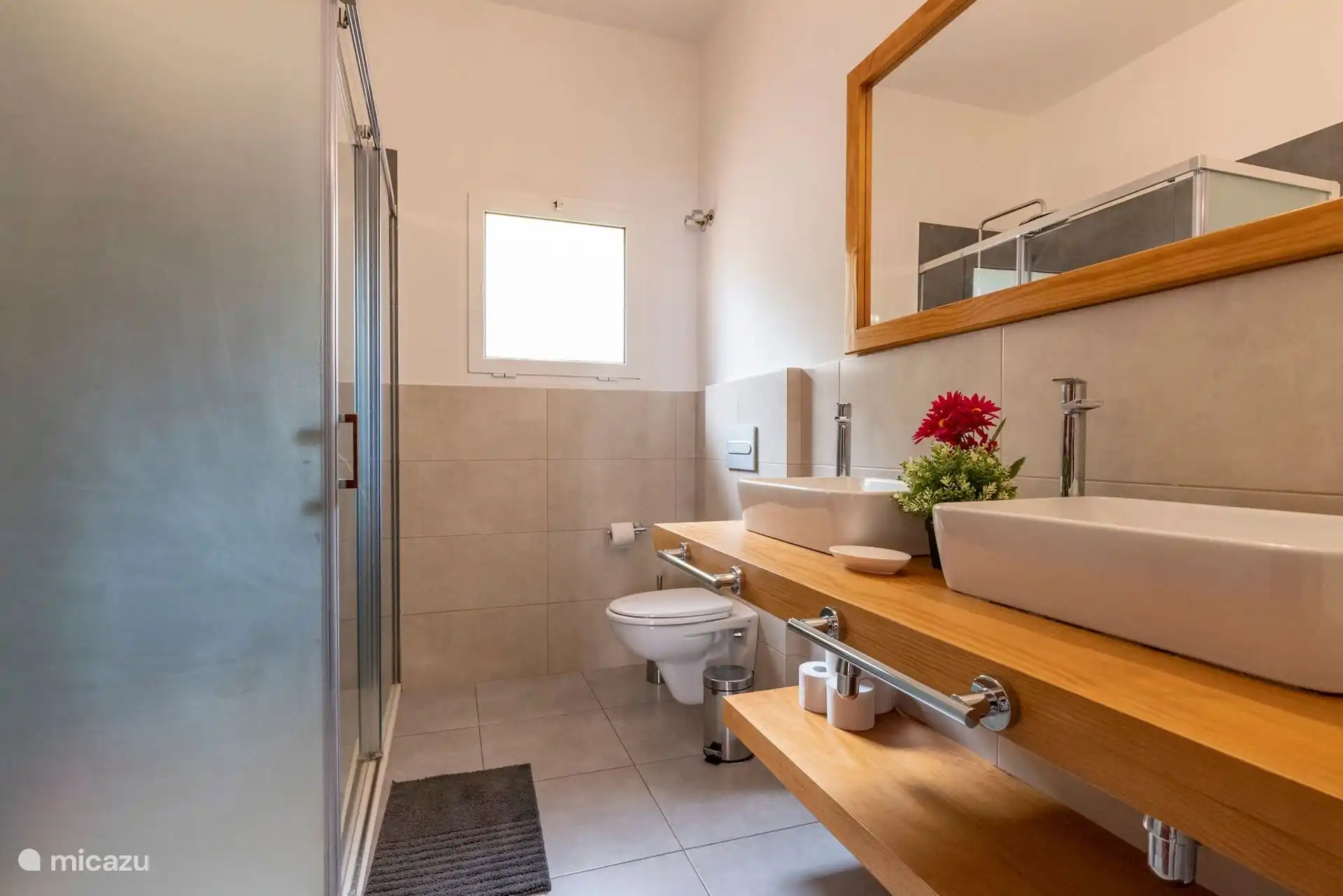 Badezimmer mit Dusche, zwei Waschbecken auf Holzablage und Fenster.