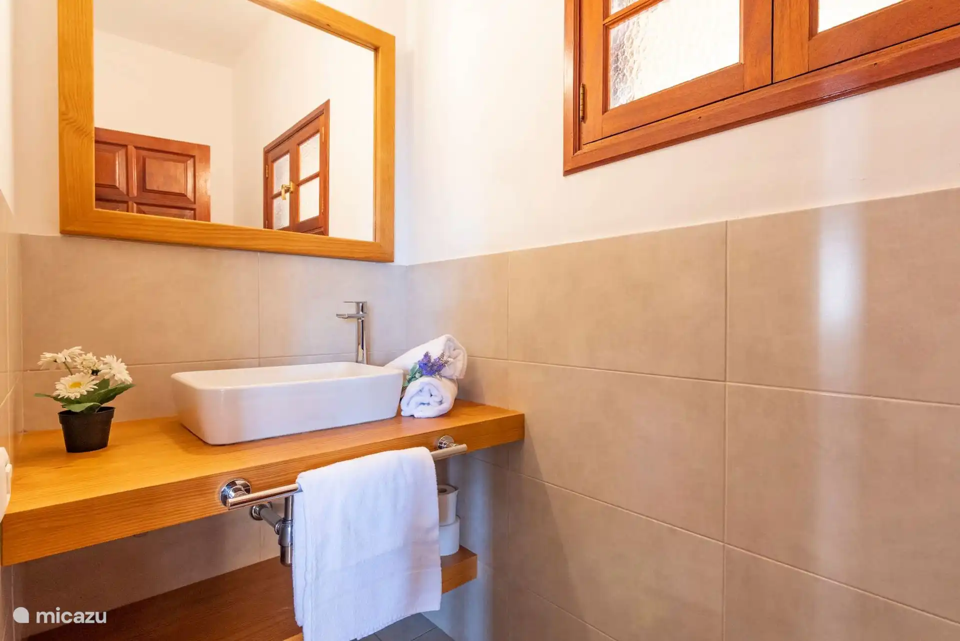 Toilette mit Waschbecken auf Holzarbeitsplatte, Spiegel und Fenster.
