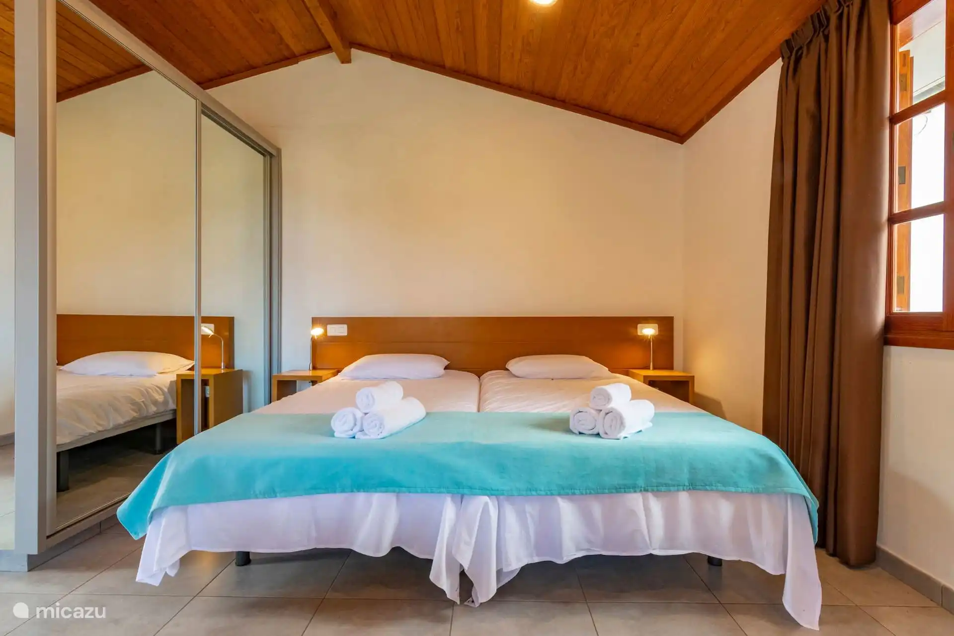 Bedroom under wooden ceiling, with mirror wardrobe and window.