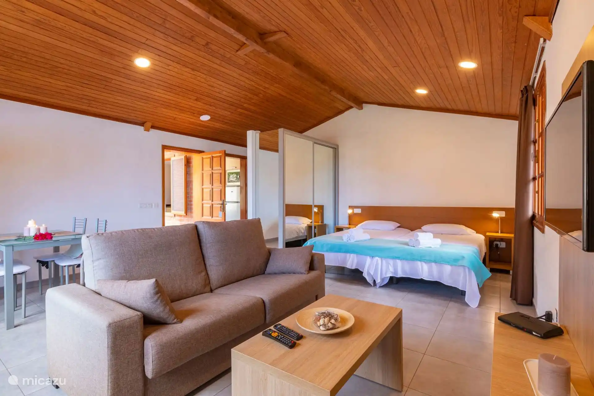 Open space: living room with sofa, dining table, television and the bed at the back.