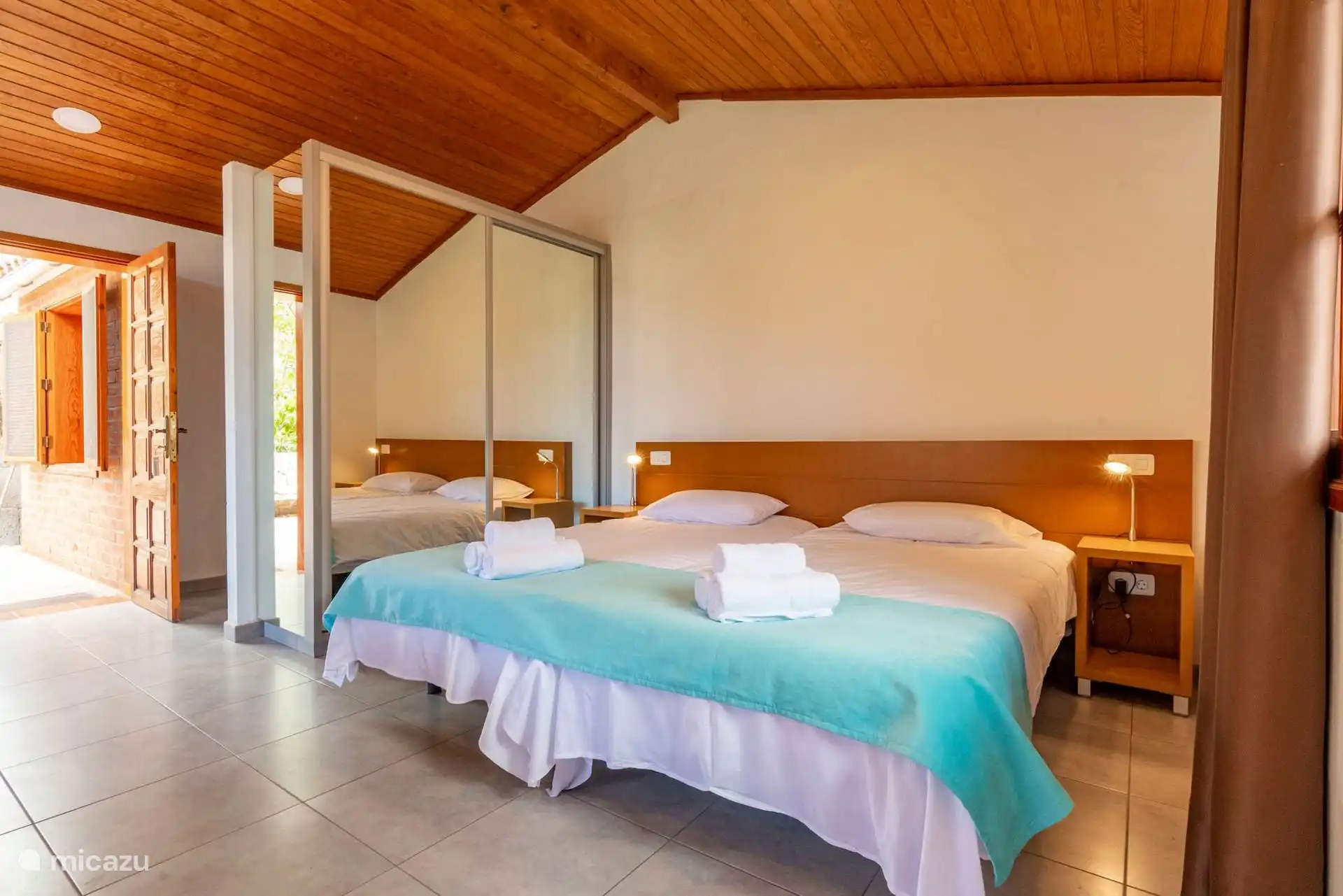 Bedroom with two single beds joined together, gabled wooden ceiling and mirrored wardrobe.