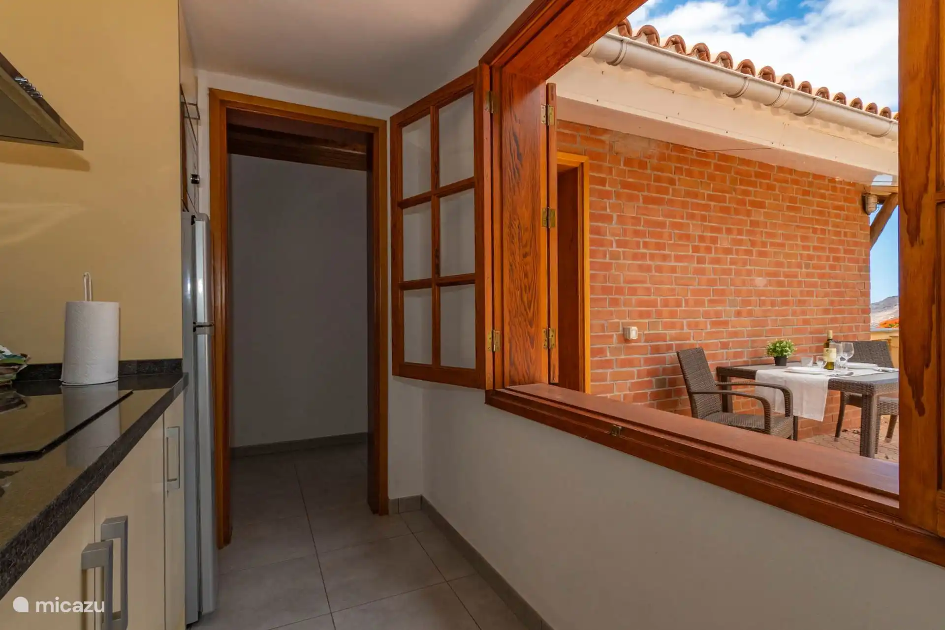 The kitchen is connected to the terrace by a small wooden window.
