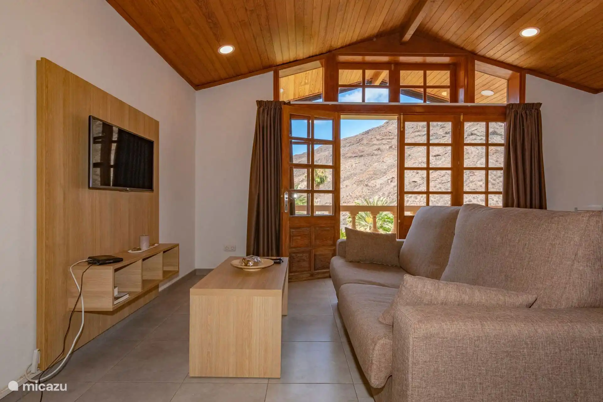 Living room with television and glass door to the balcony, with mountain views.