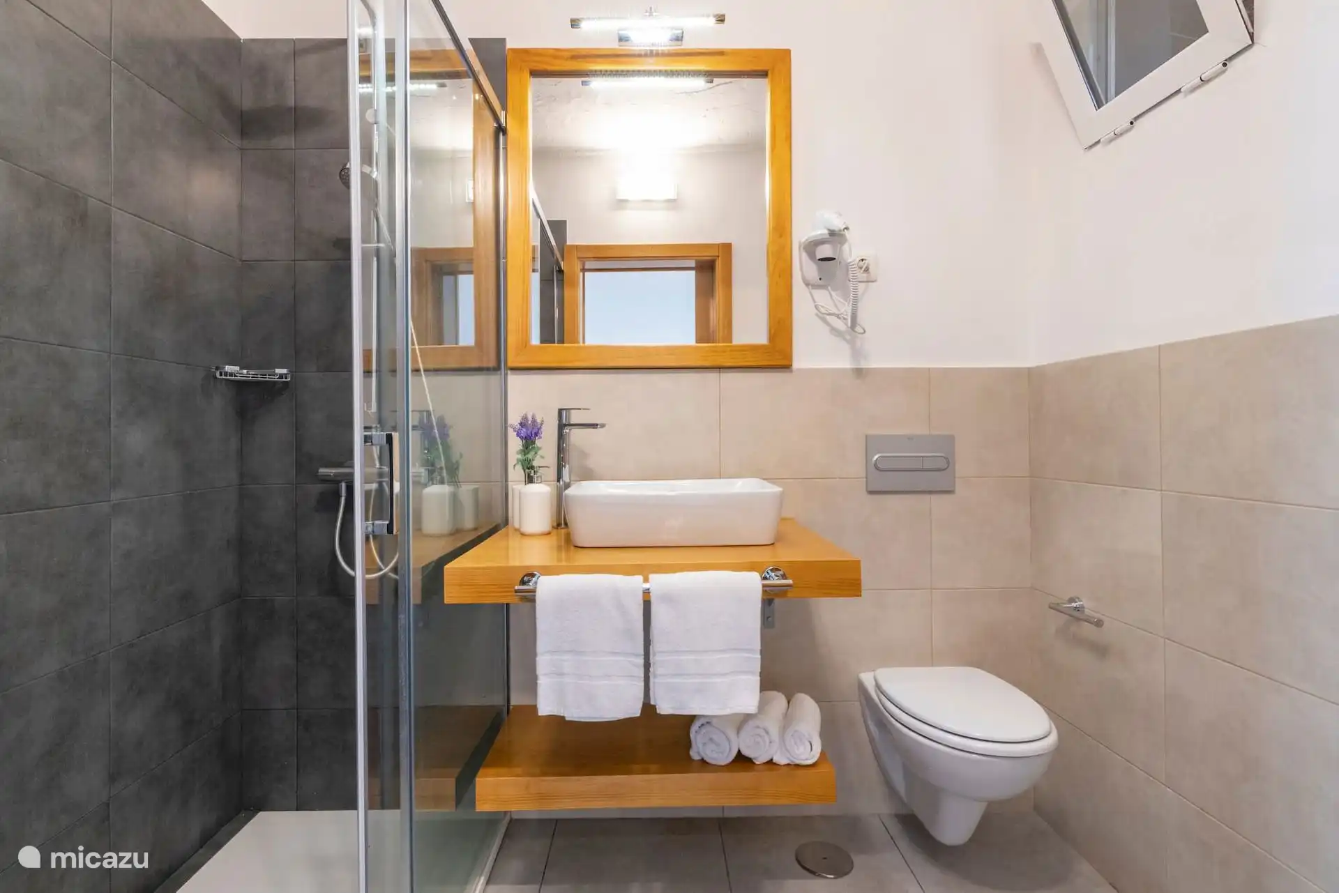 Badezimmer mit glasierter Dusche, Waschbecken auf Holzarbeitsplatten und Föhn.