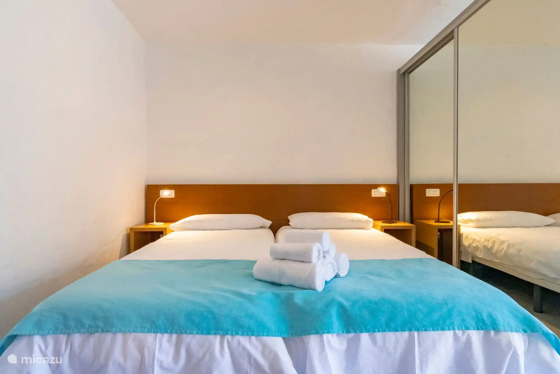 Schlafzimmer mit zwei miteinander verbundenen Einzelbetten und Kleiderschrank mit Spiegel.
