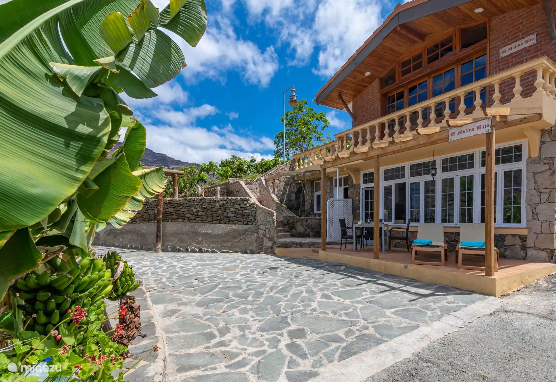 Das Haus von der Terrasse aus: verglaste Galerie, Terrasse und Bananenbäume drumherum.