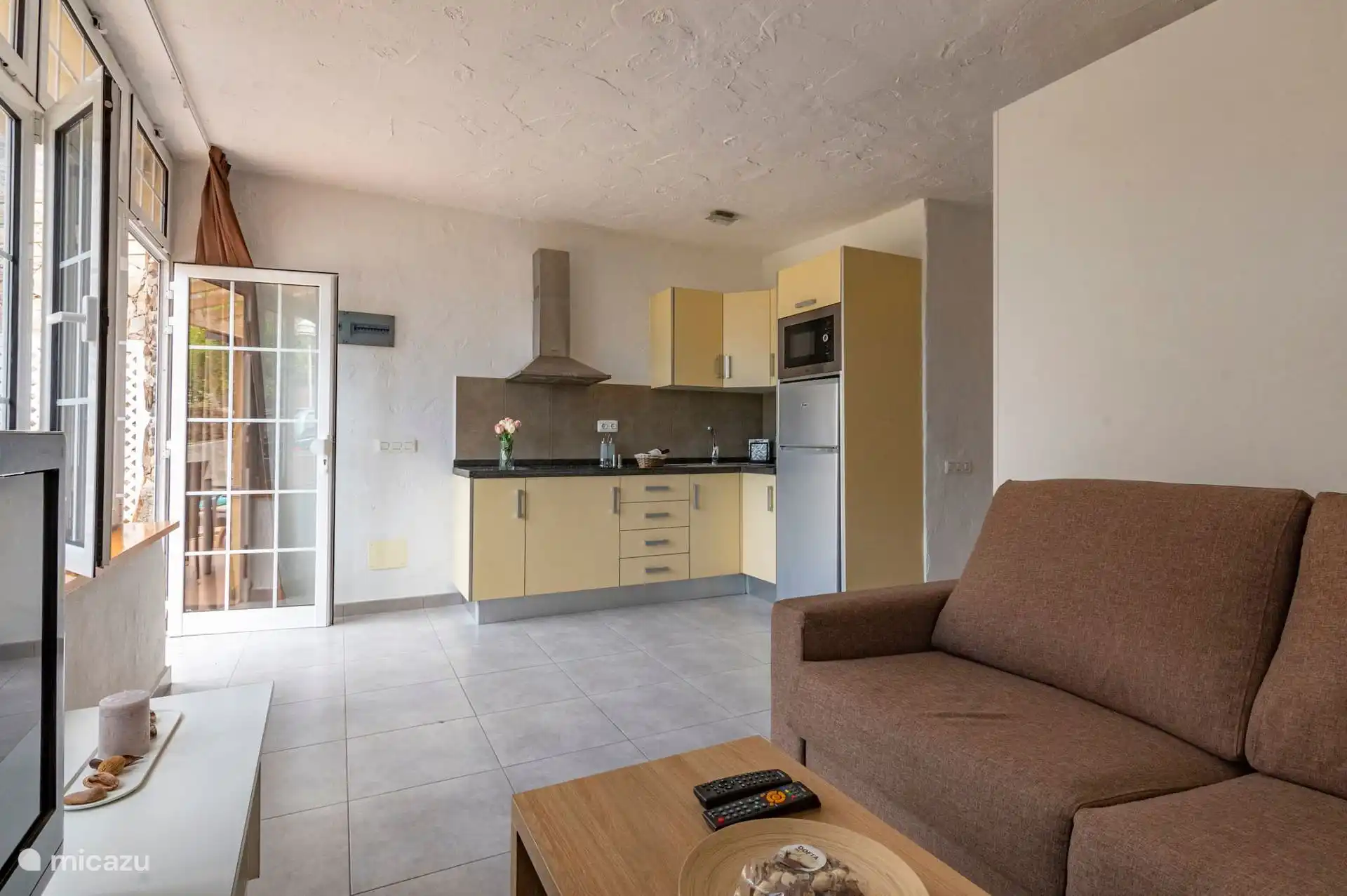 Wohnzimmer mit Sofa und direktem Zugang zur Terrasse; Im Hintergrund die Küche.