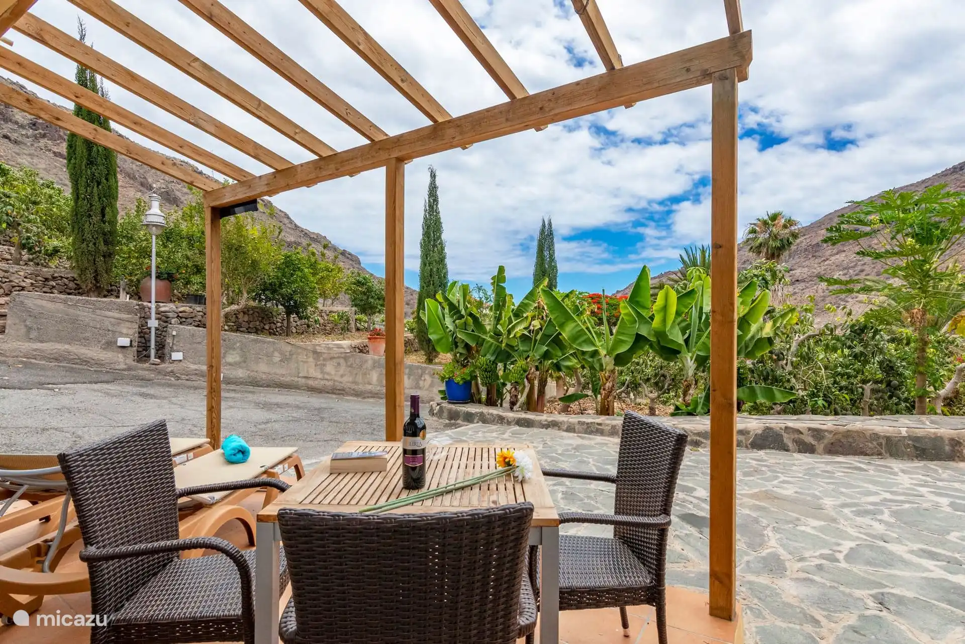 Tisch und Stühle unter der Pergola, mit Blick auf die Bananenbäume und die Berge.