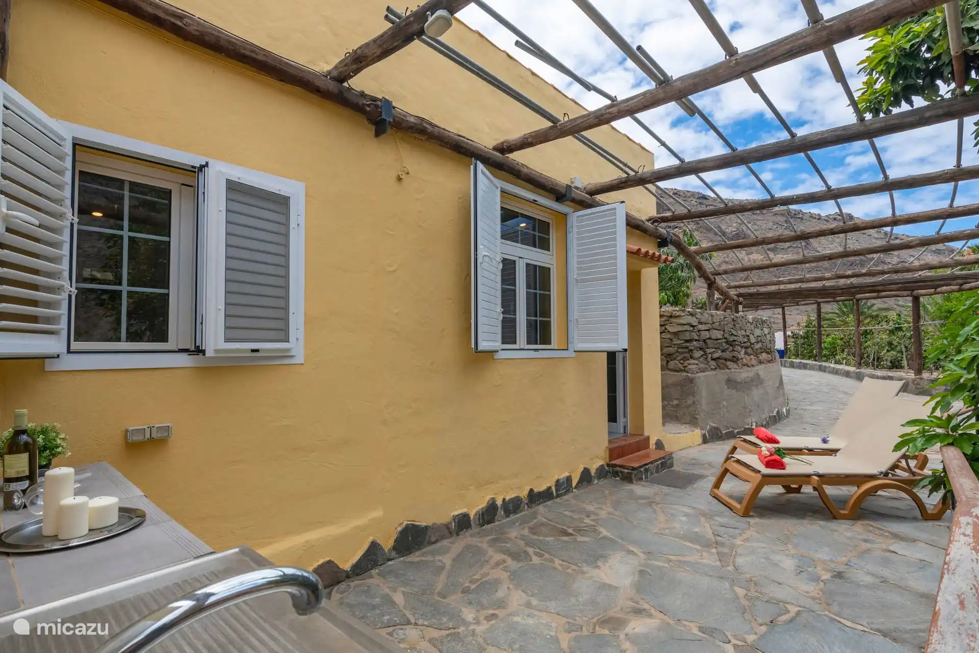 Fassade des Hauses und gepflasterte Terrasse unter der hölzernen Pergola.