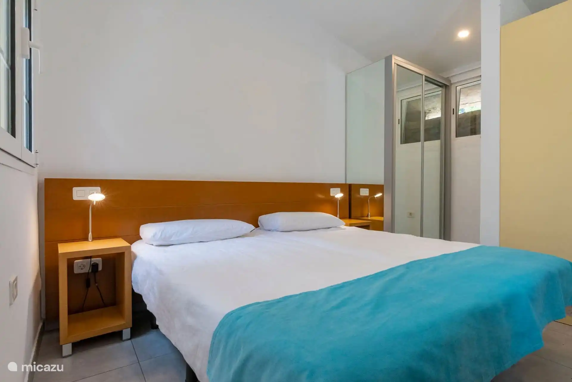 Schlafzimmer mit zwei aneinandergebauten Einzelbetten, Nachttische und Kleiderschrank mit Spiegel.