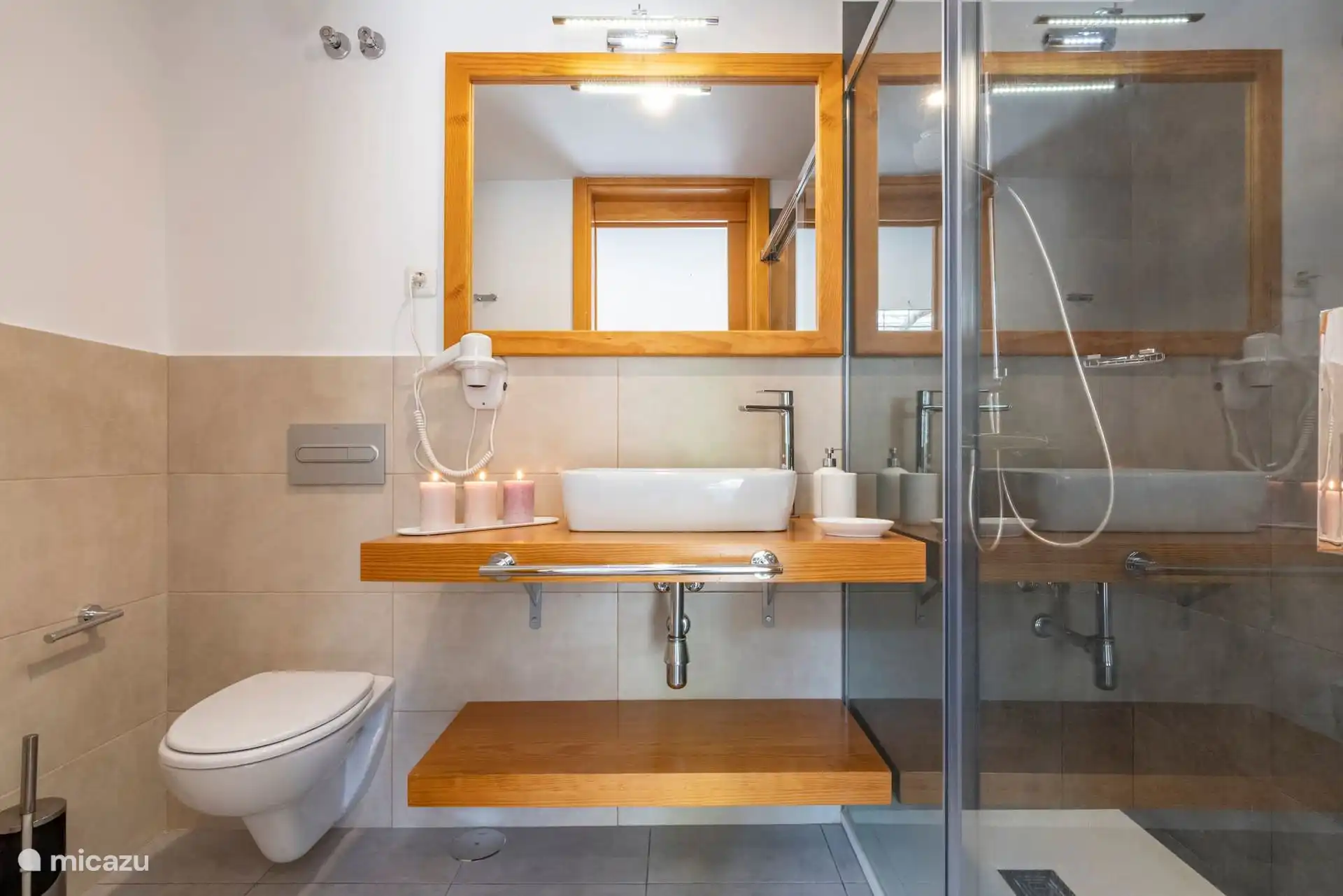 Badezimmer mit glasierter Dusche, Waschbecken auf Holzarbeitsplatten und Föhn.
