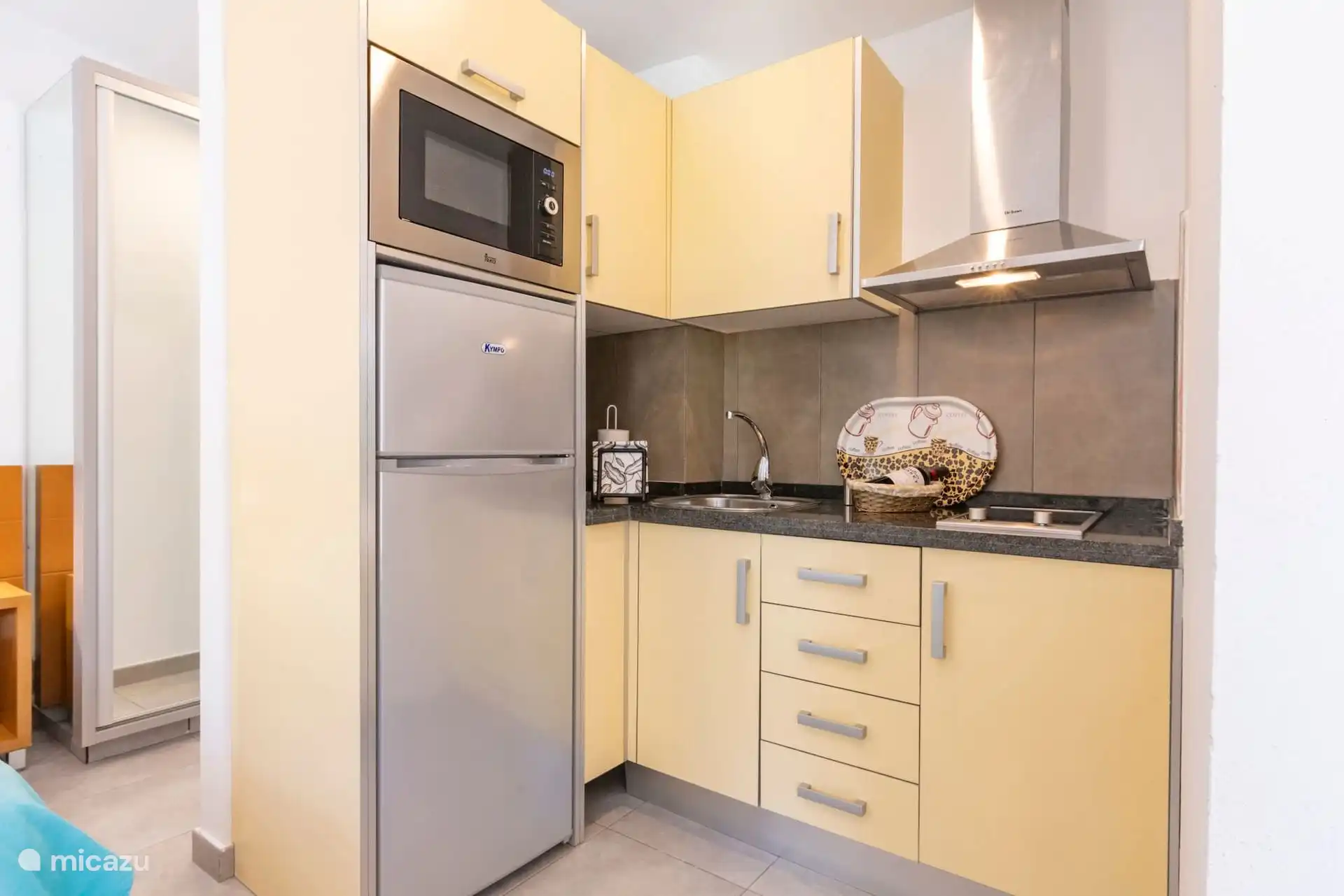 Küche ausgestattet mit Kühlschrank, Mikrowelle, Dunstabzugshaube, Spüle und Keramikherd.