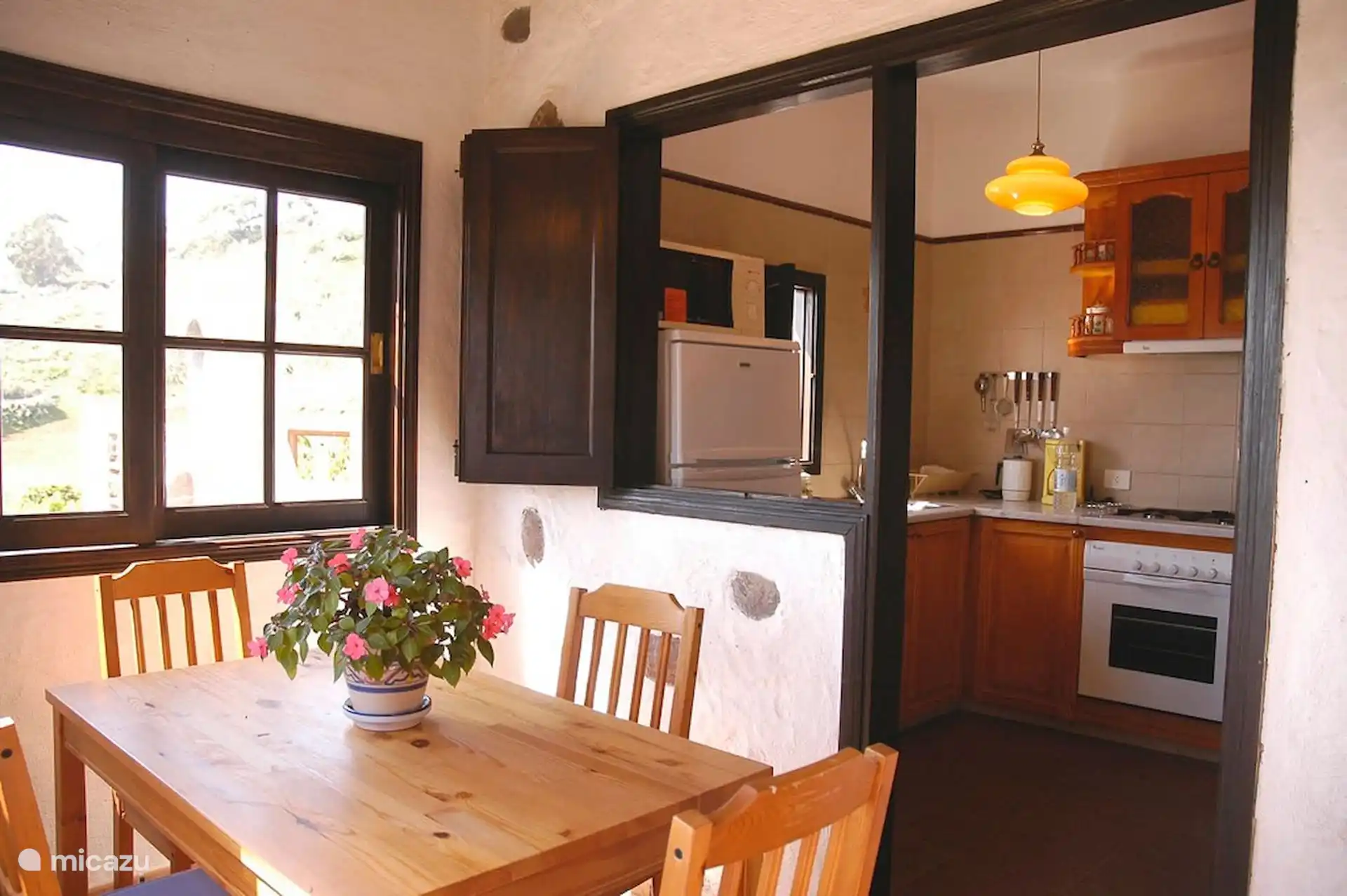 Eetkamer met houten tafel en achterin de aparte keuken met oven, gasfornuis en koelkast.