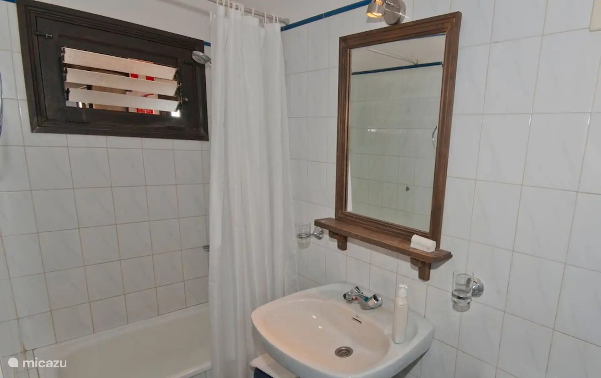 Badkamer met badkuip, wastafel en spiegel; raam met houten traliewerk.