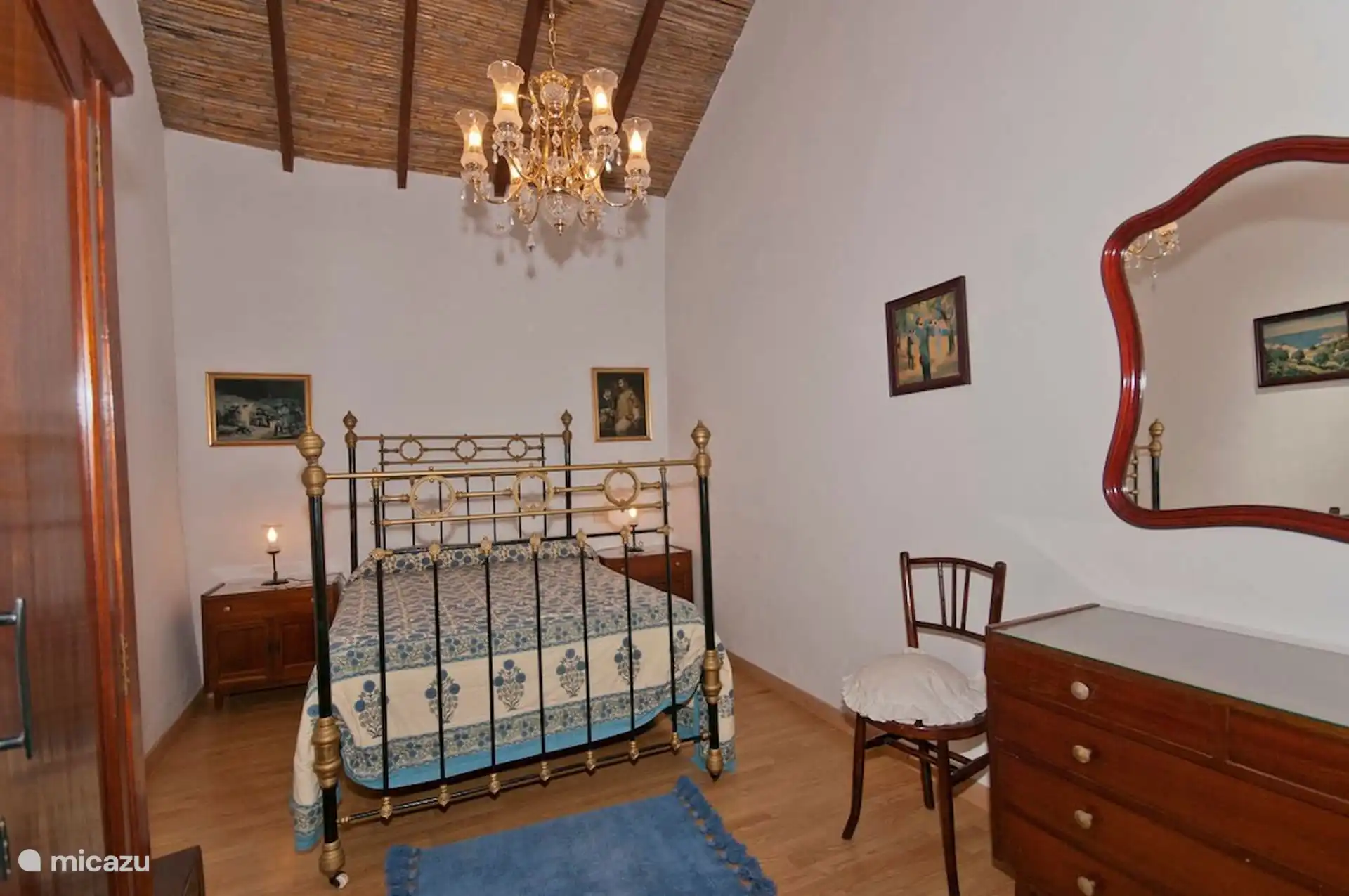 Slaapkamer met smeedijzeren tweepersoonsbed, ladekast met spiegel en riet dak.