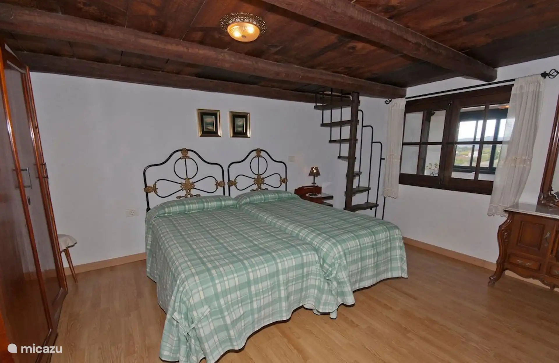 Slaapkamer met twee eenpersoonsbedden, smeedijzeren hoofdborden, kledingkast en raam naar het platteland.