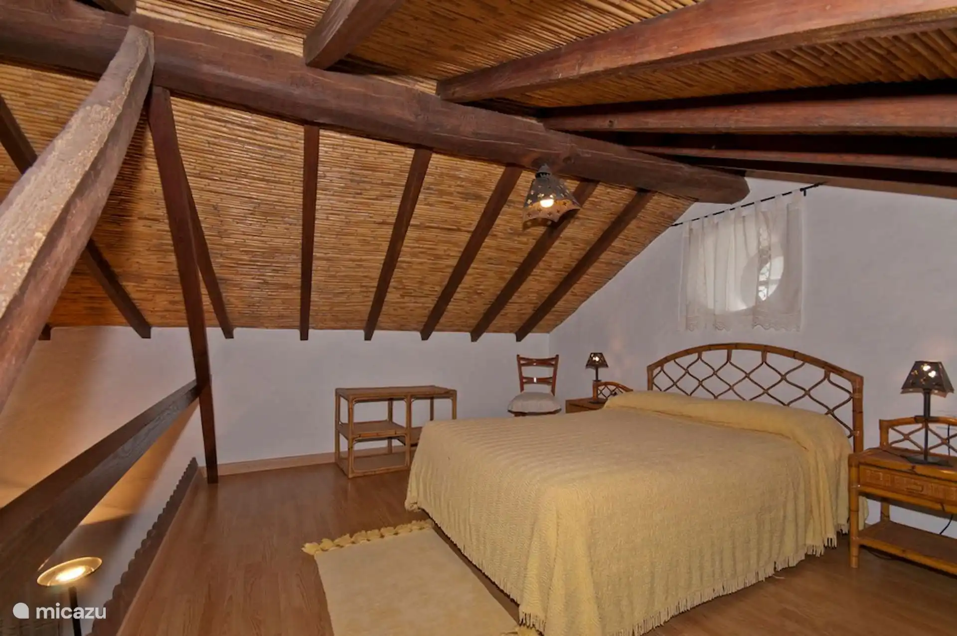 Zolderloft met tweepersoonsbed, rietplafond en zichtbare houten balken.