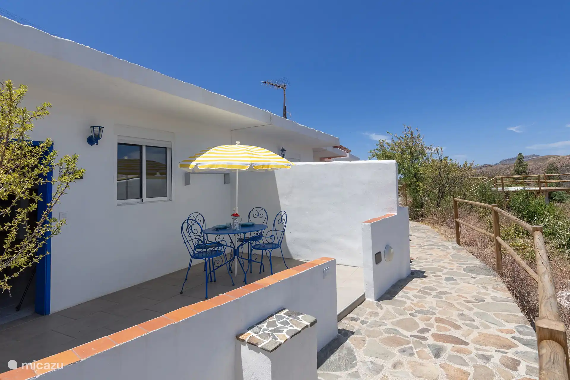 Private Terrasse mit Tisch, Stühlen und Sonnenschirm, neben dem Eingang.