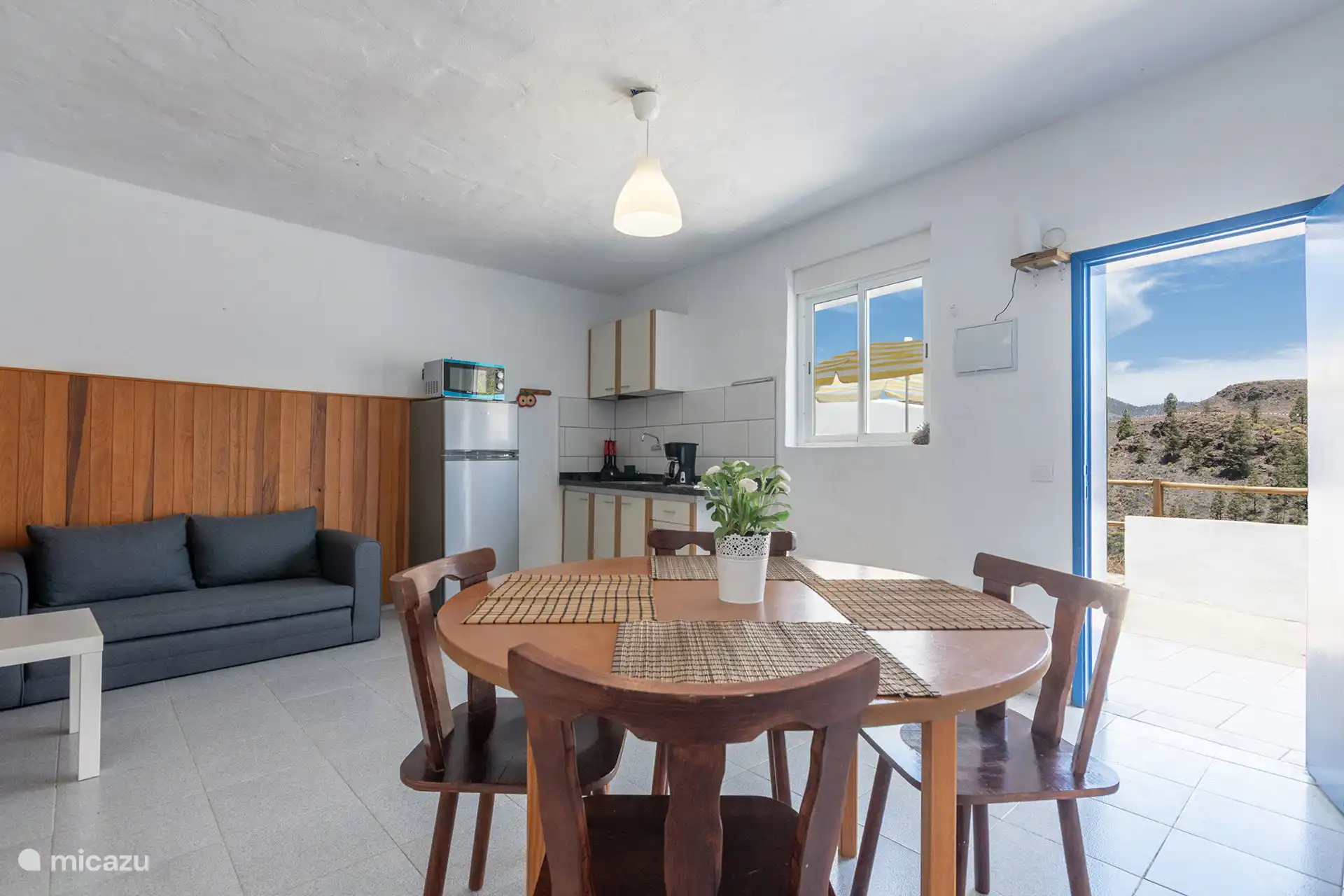 Wohnzimmer mit Schlafsofa, rundem Tisch, integrierter Küche und Zugang zur Terrasse.