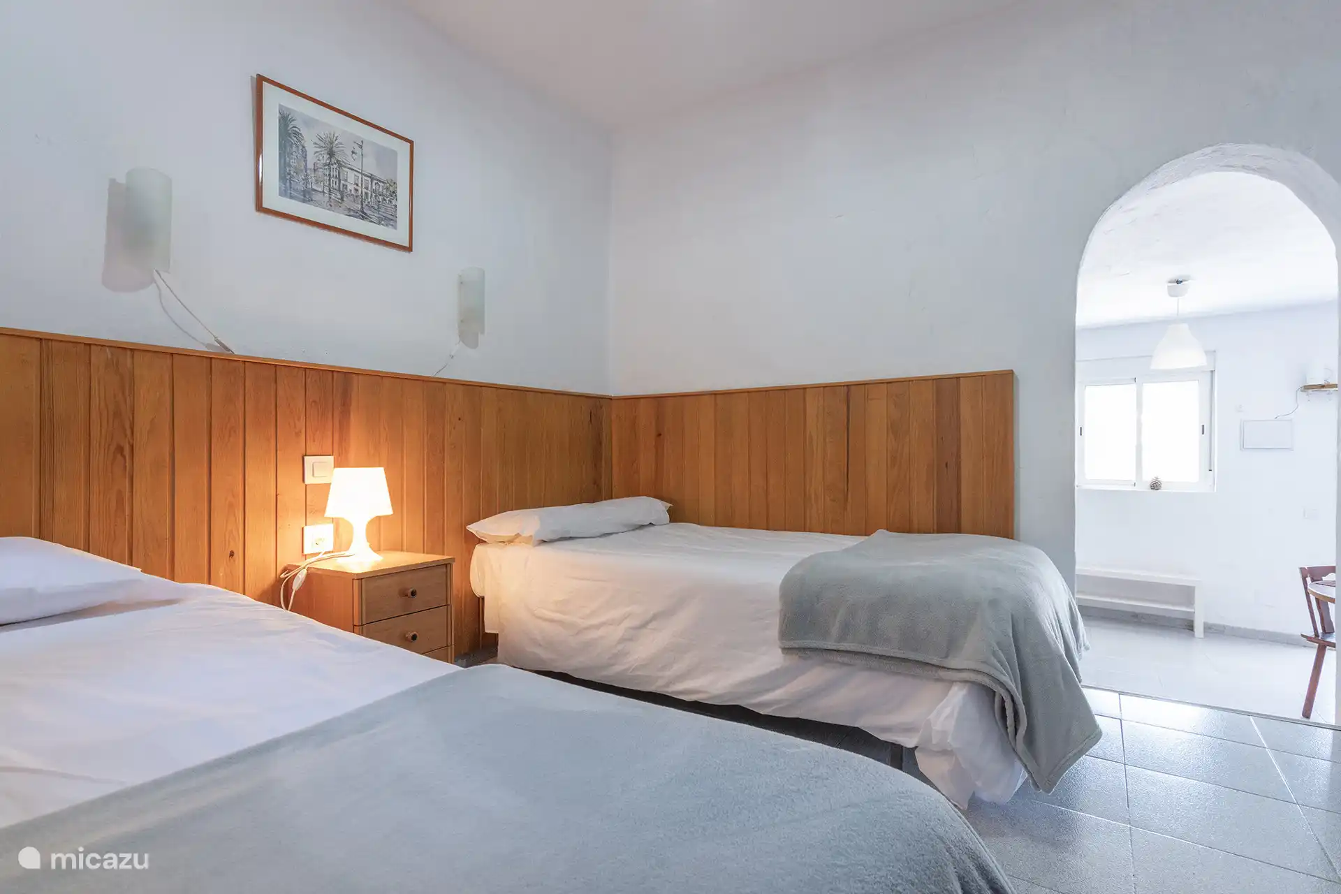 Schlafzimmer mit zwei Betten, Nachttisch und Torbogen öffnen sich zum Wohnzimmer.