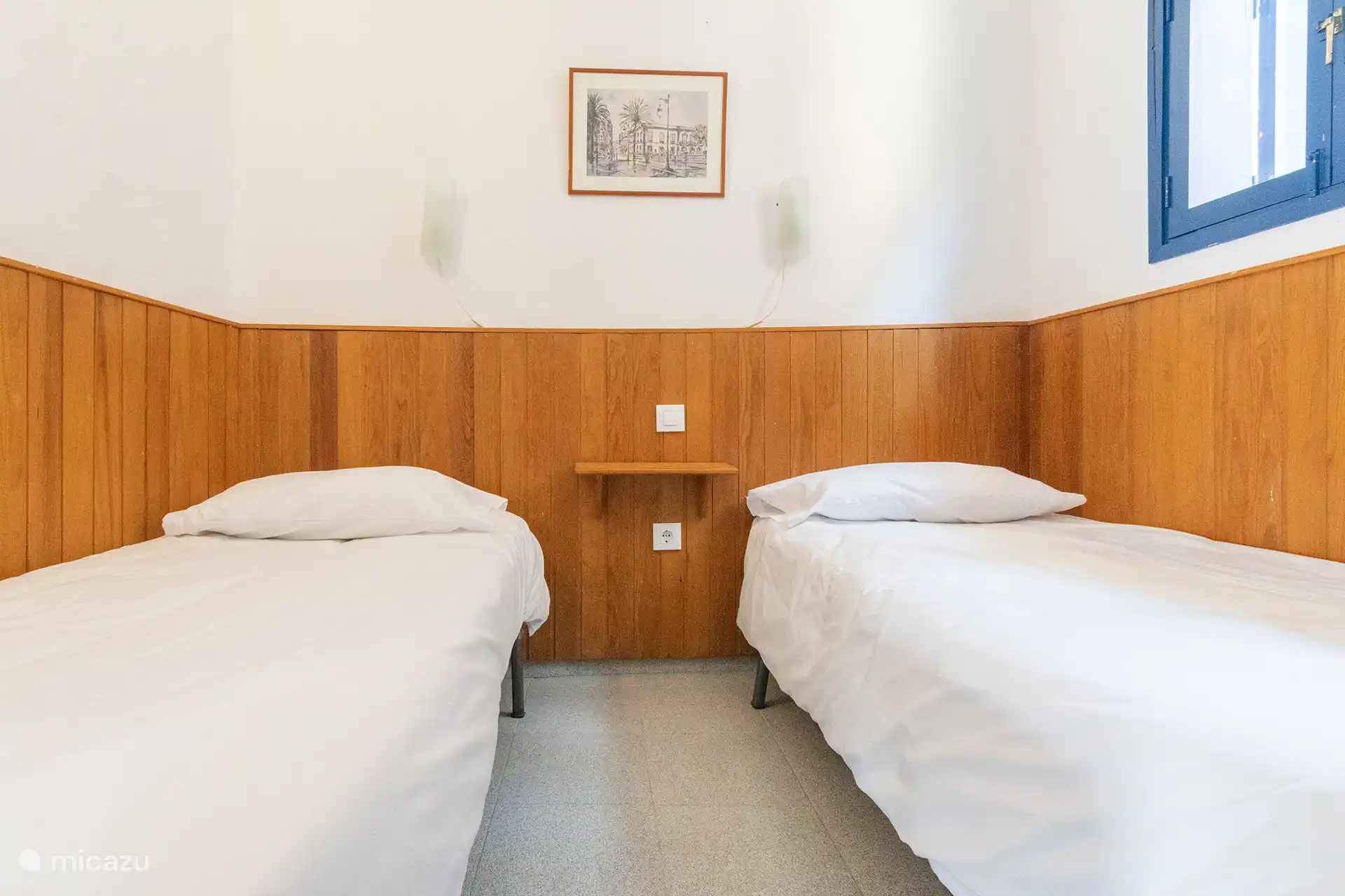 Slaapkamer met twee eenpersoonsbedden, houten sokkel en raam.
