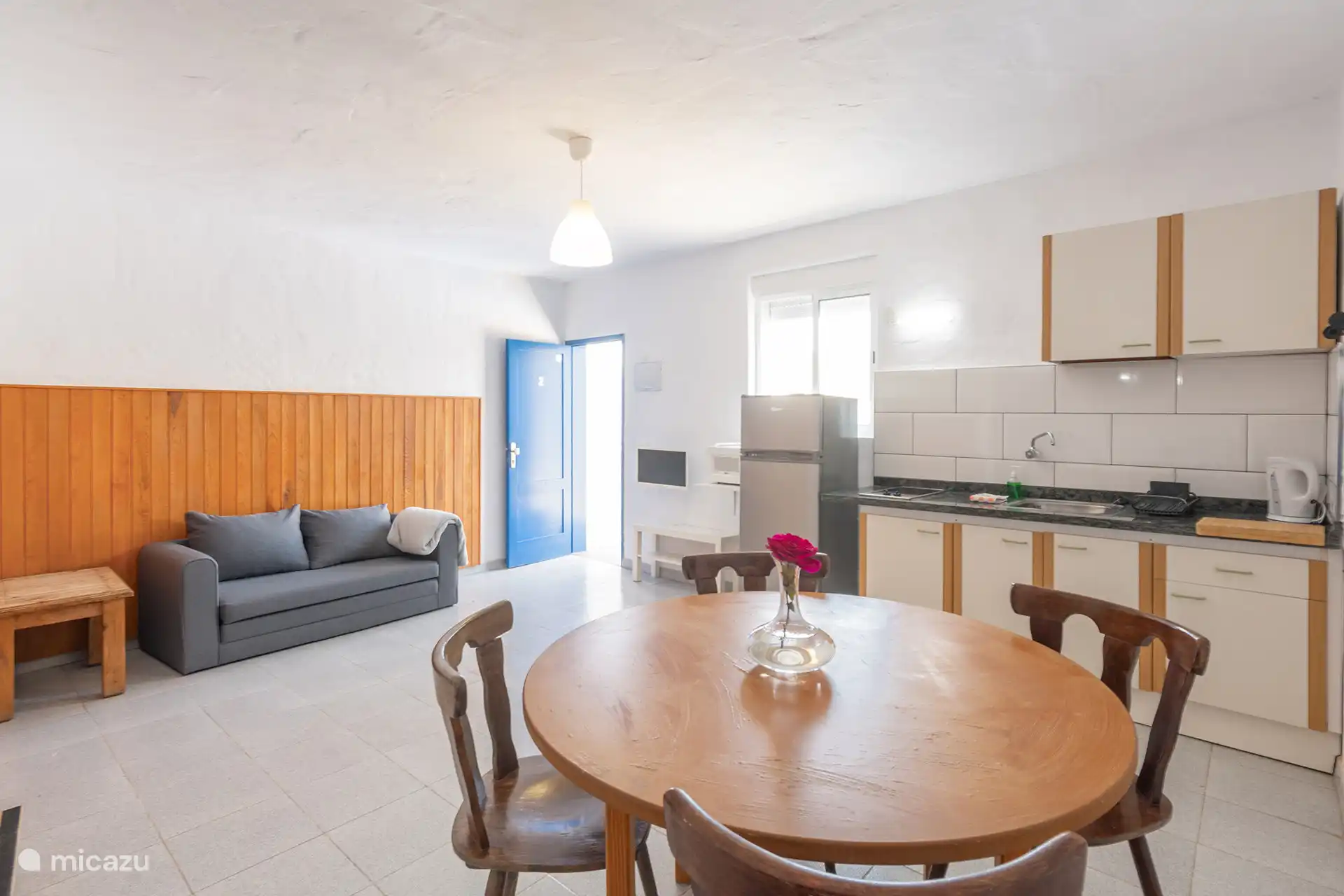 Woonkamer met slaapbank, ronde tafel en de geïntegreerde keuken naast de ingang.