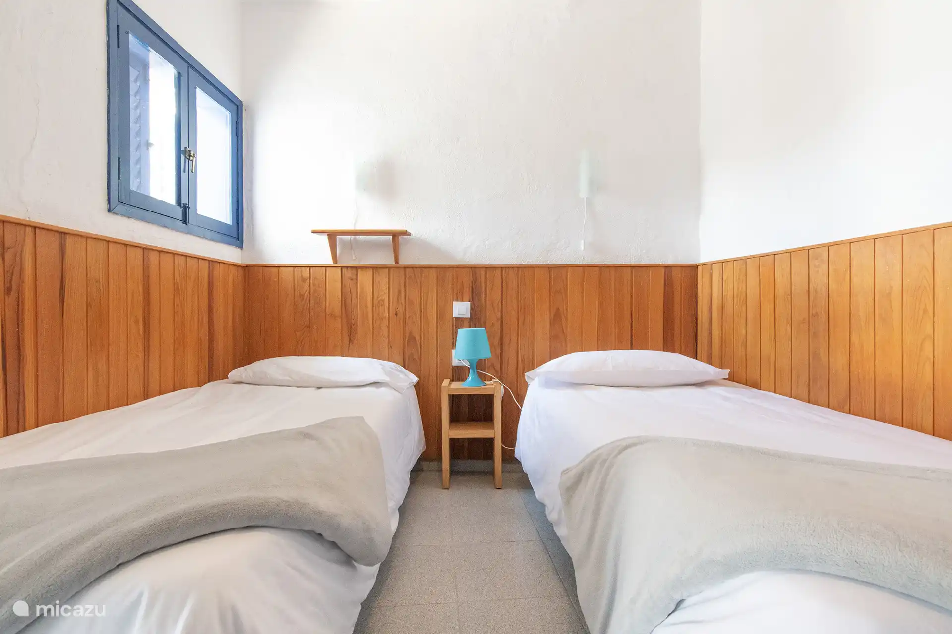Bedroom with two single beds, wooden plinth and window.