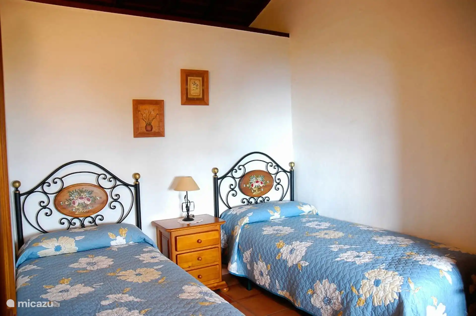 Schlafzimmer mit zwei Einzelbetten und schmiedeeisernen Kopfteilen mit bemaltem Medaillon.