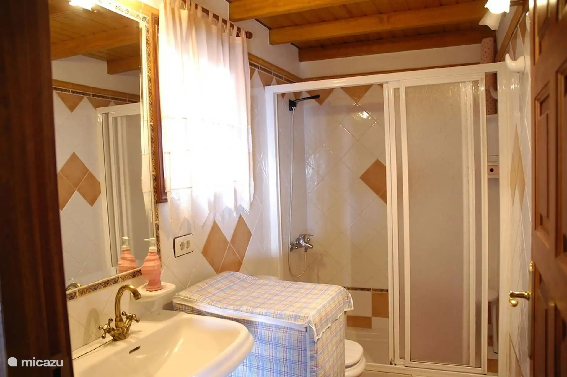 Badkamer met douchescherm, wastafel en raam; houten plafond.